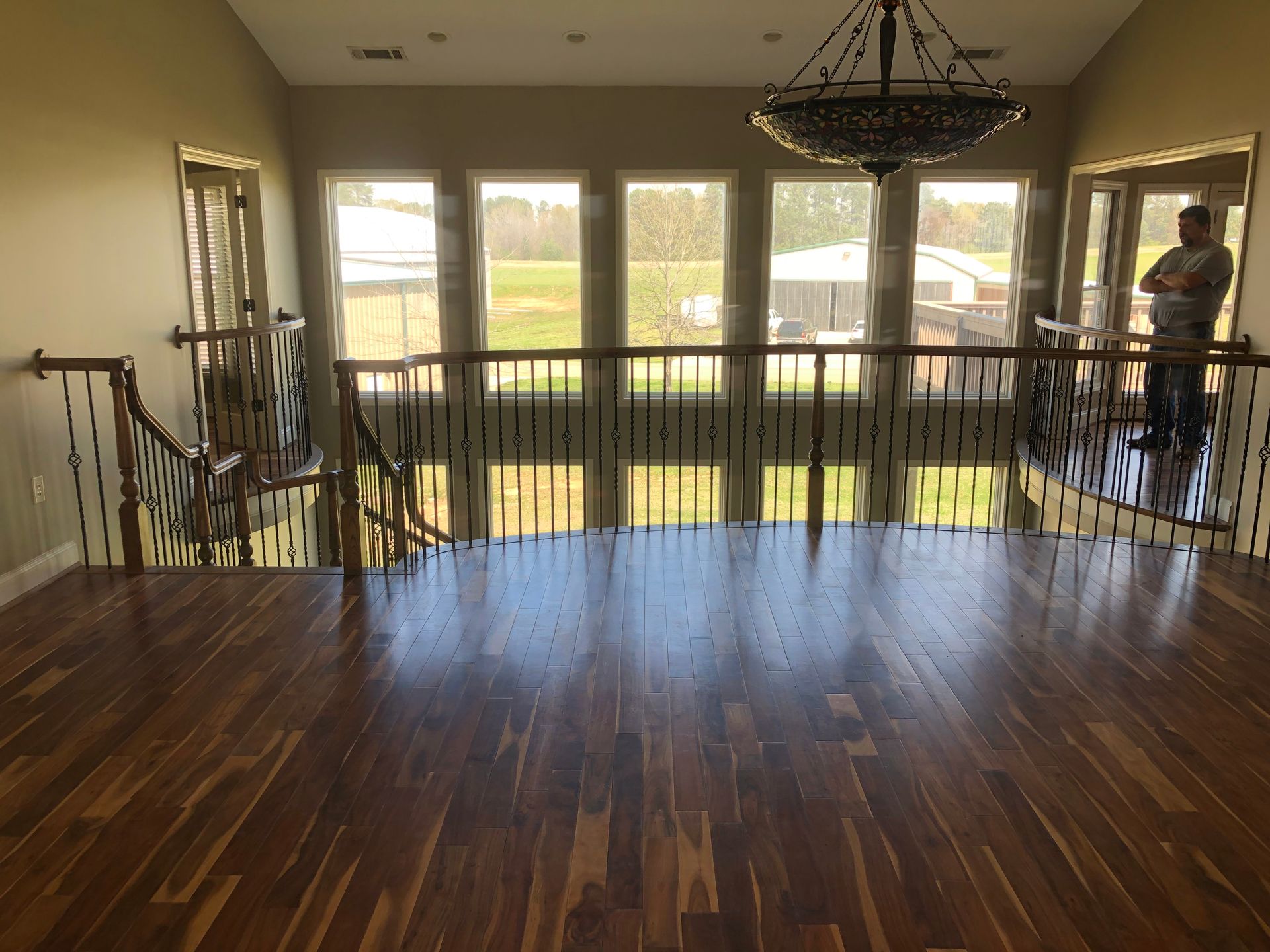 Spacious room with hardwood floor, chandelier, and large windows overlooking a field.