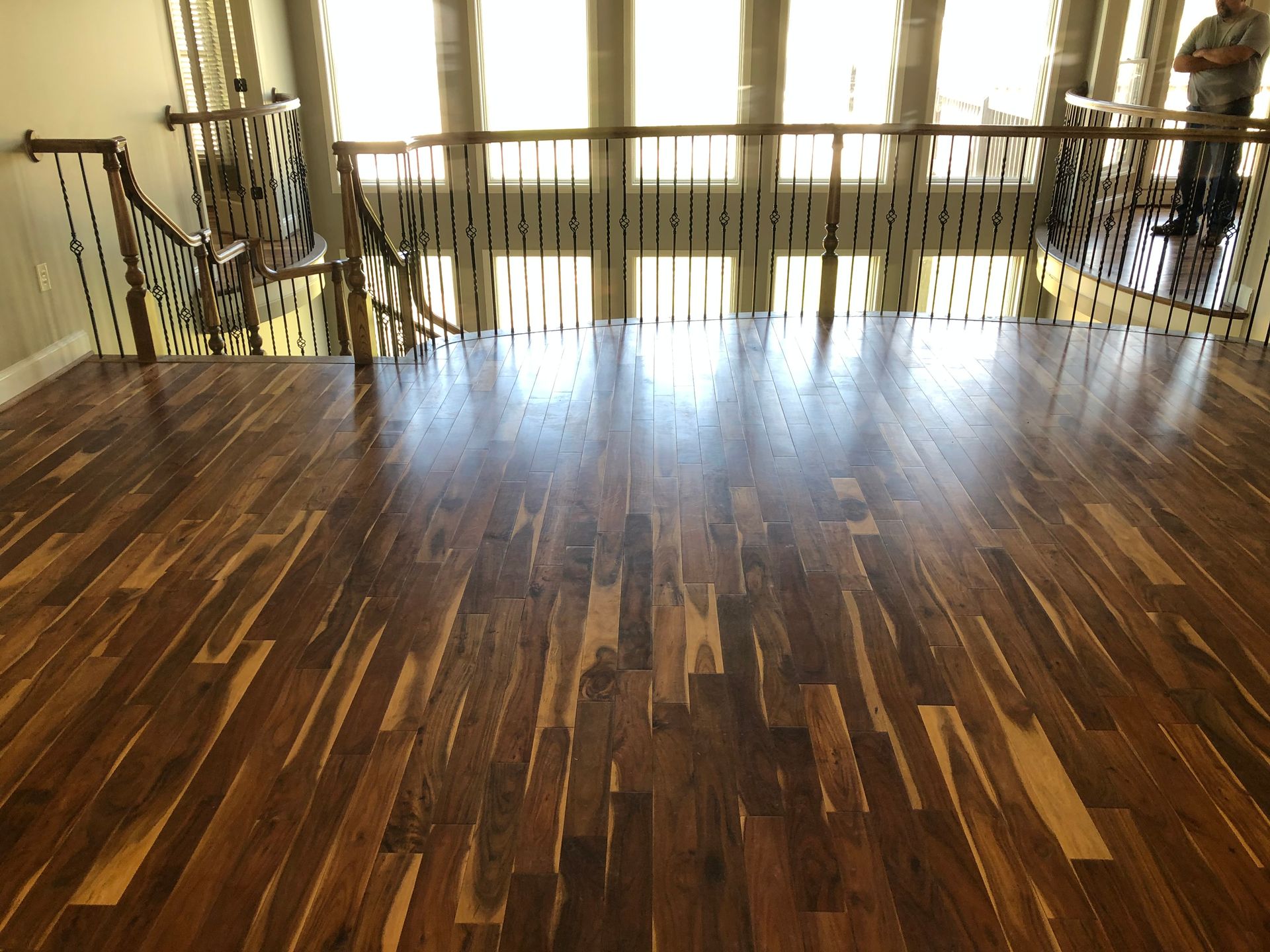 Empty polished wooden room with railings and bright windows at the back.
