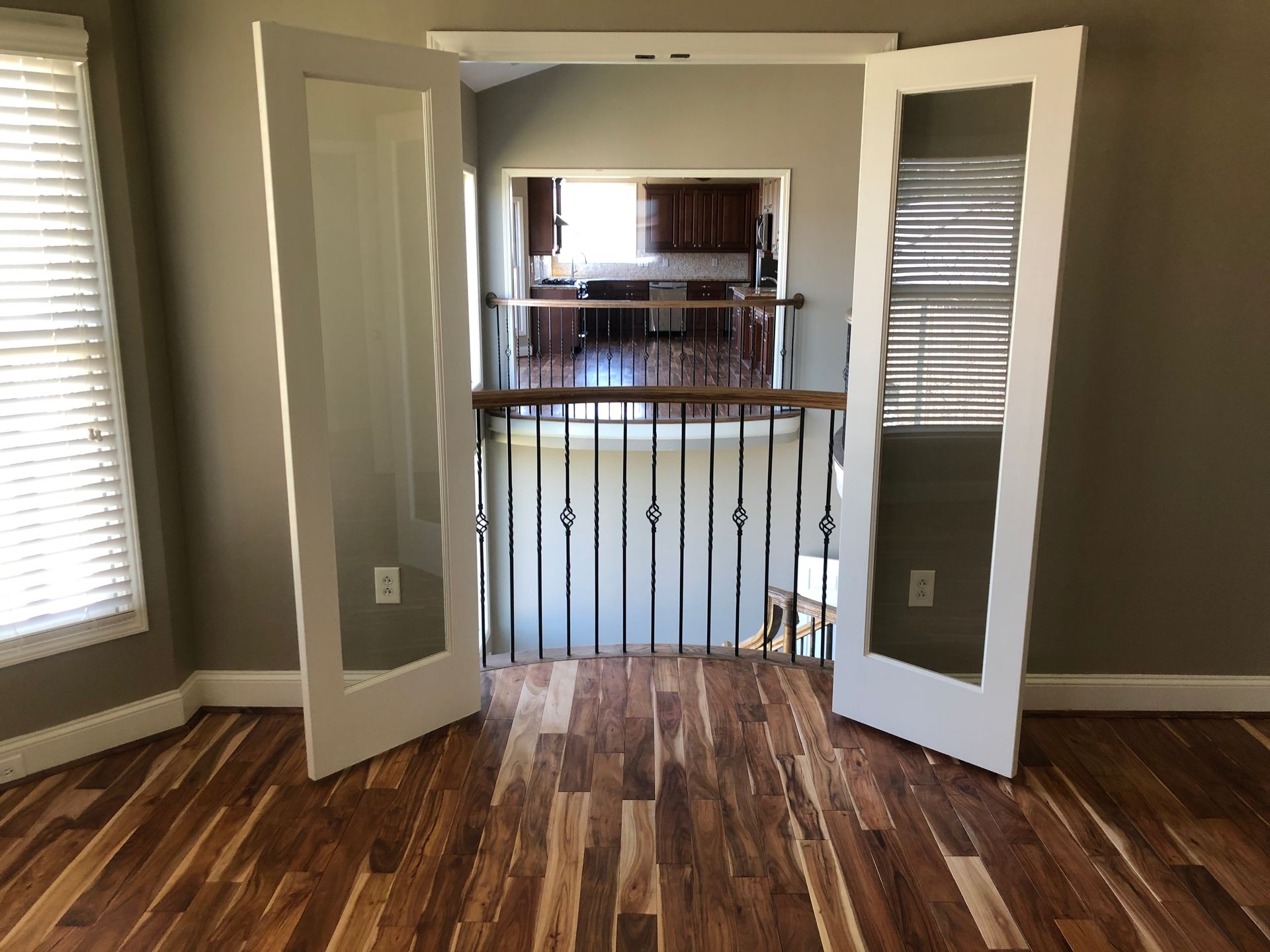 Open double doors to a hallway with wood floors and a black railing overlooking a lower level