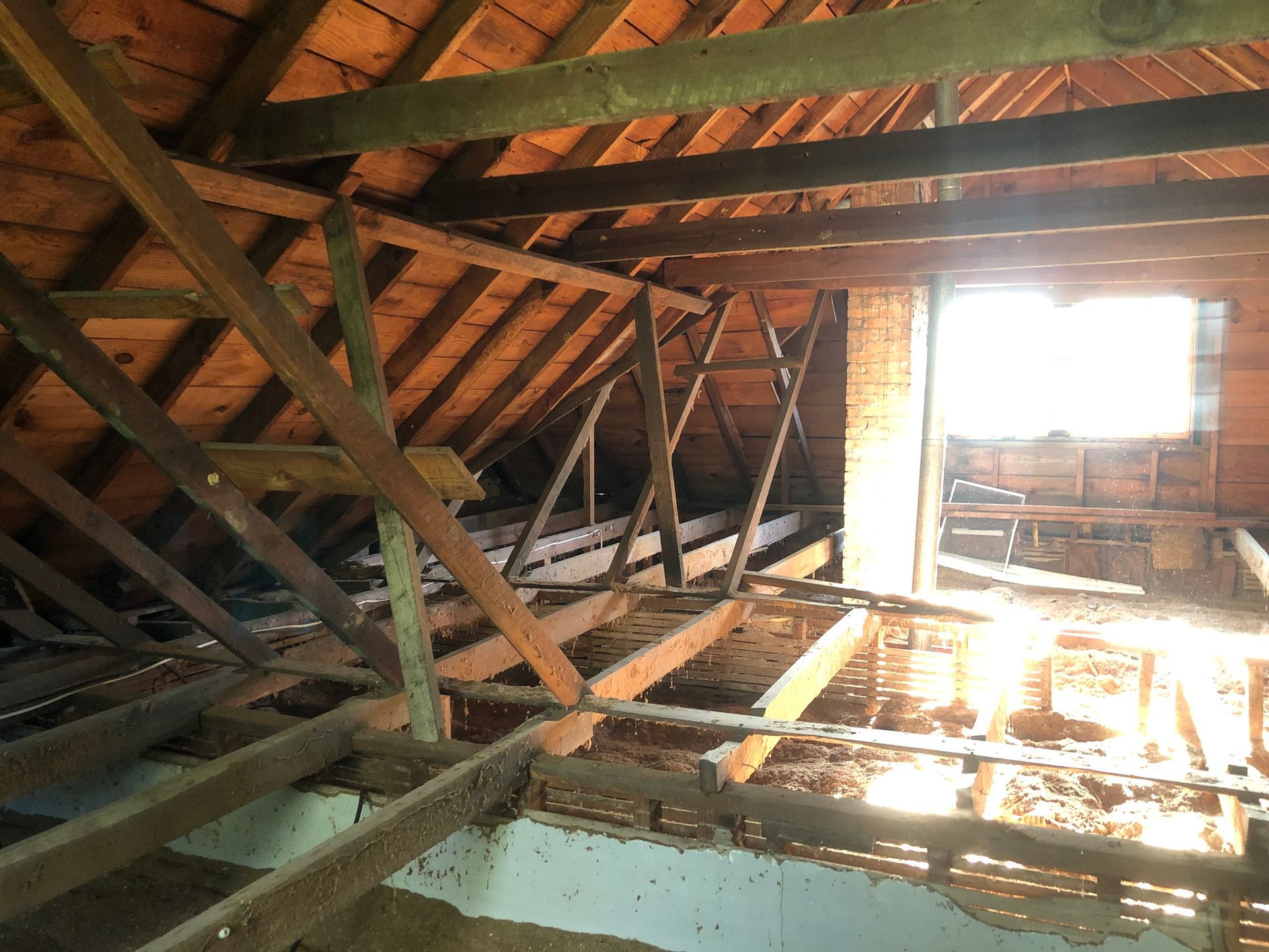 Attic interior with exposed wooden beams and bright sunlight through a window opening