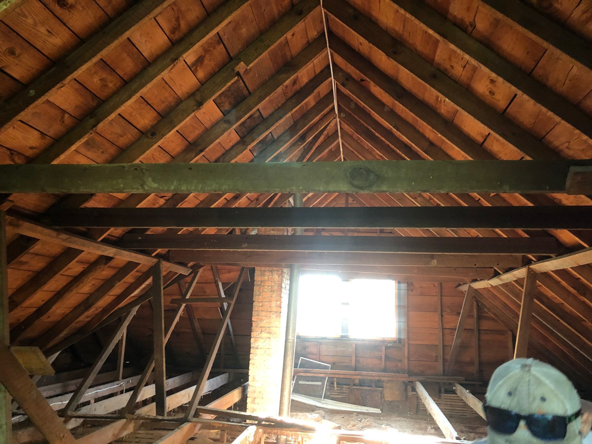 Attic with exposed wooden rafters, brick walls, and a bright window at the far end.