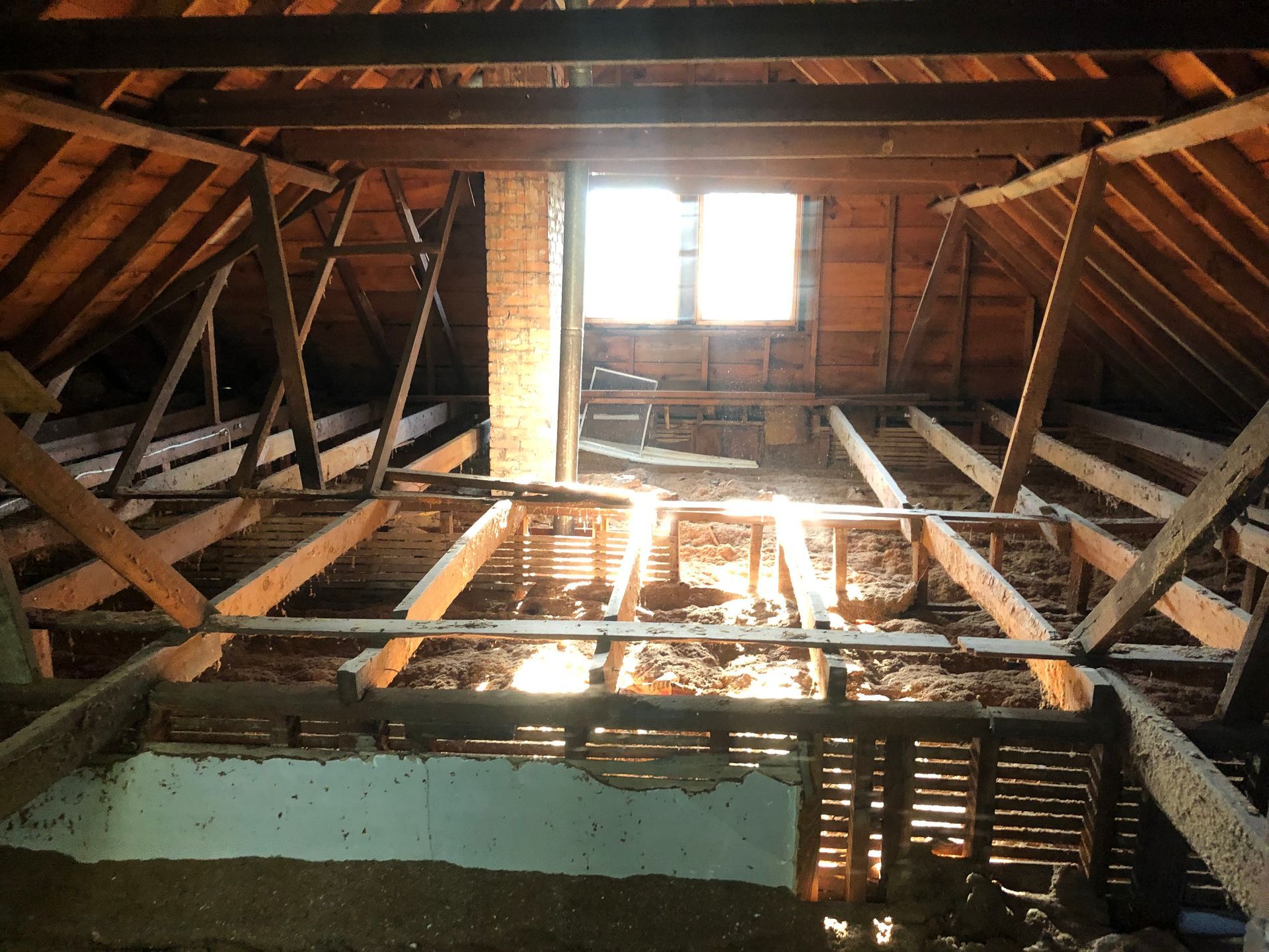 Damaged attic with exposed wooden rafters and a broken ceiling around a bright window opening