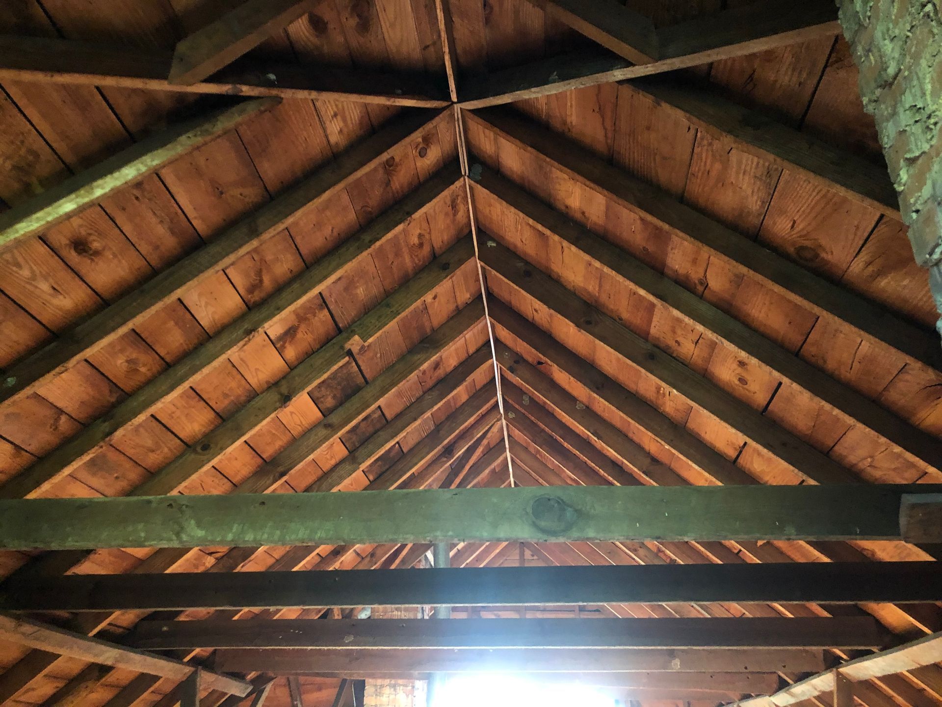 Wooden cabin ceiling with exposed beams and bright light shining through the center seam