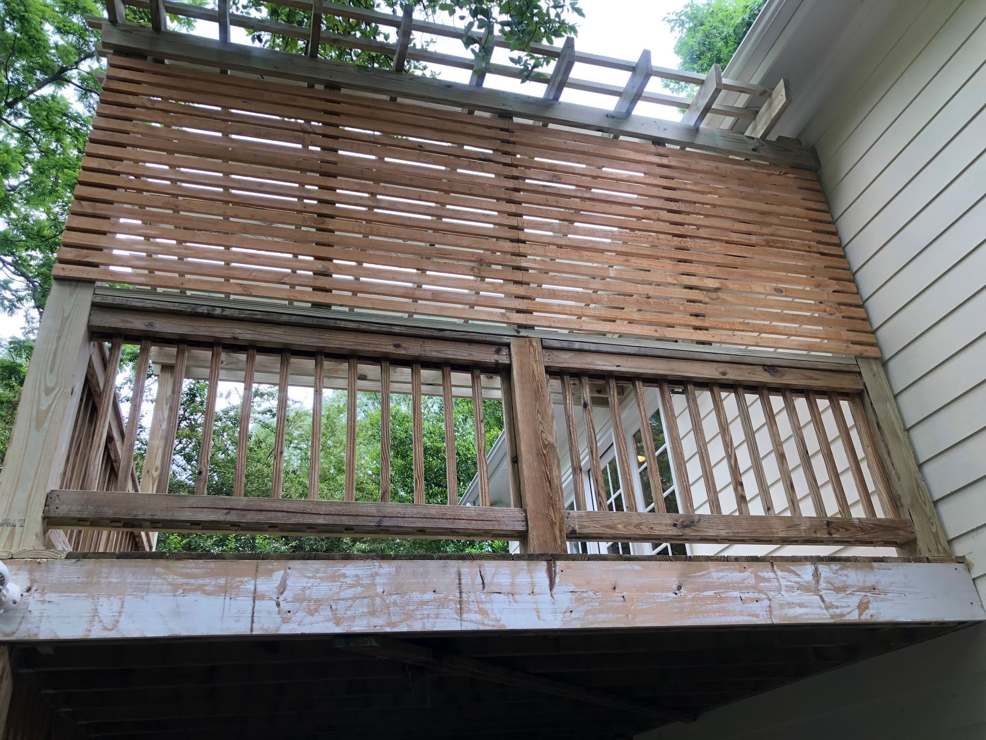 Wooden deck with slatted privacy screen and railing attached to a house exterior