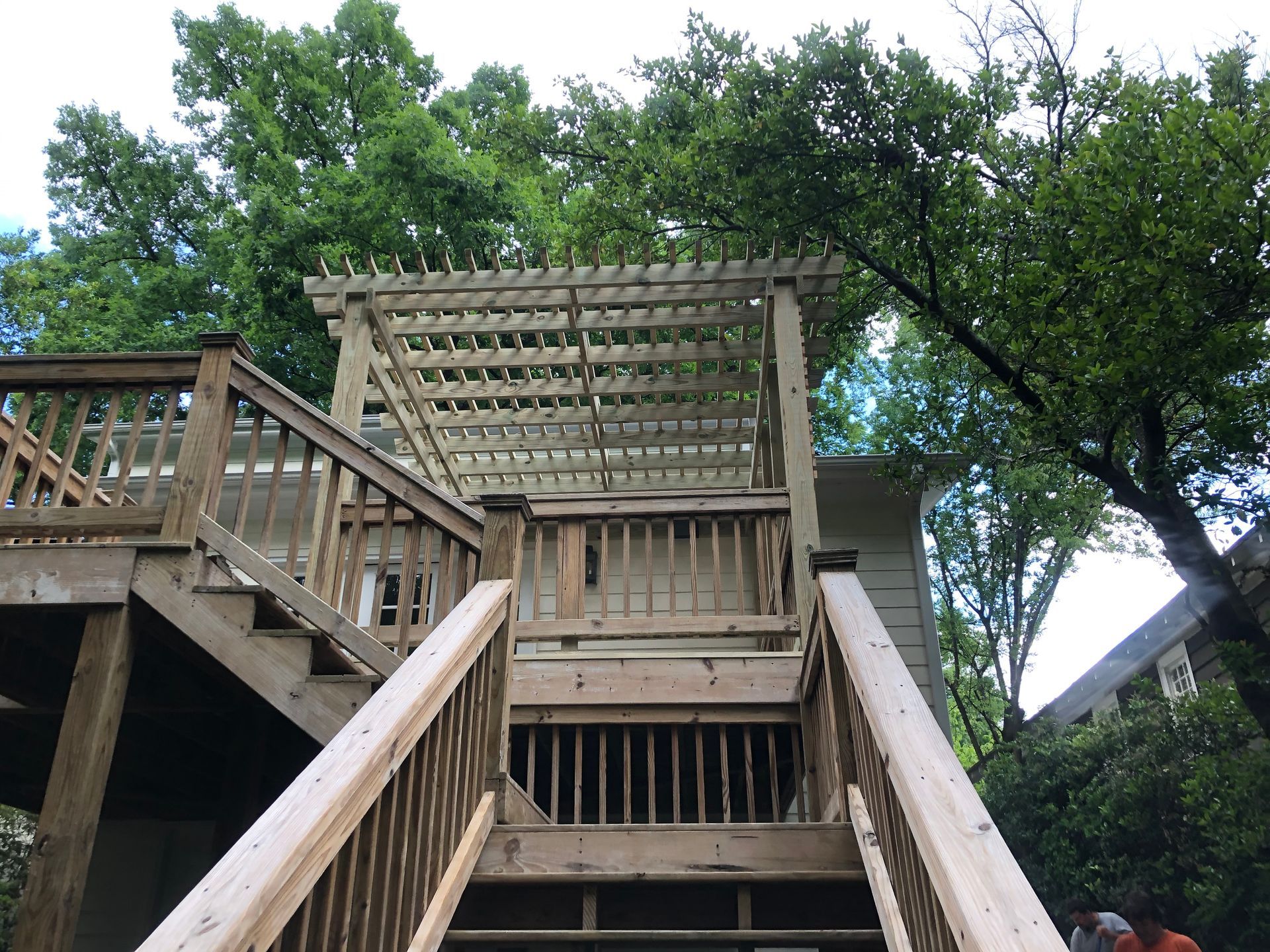 Wooden deck stairs leading to a pergola, surrounded by trees and greenery