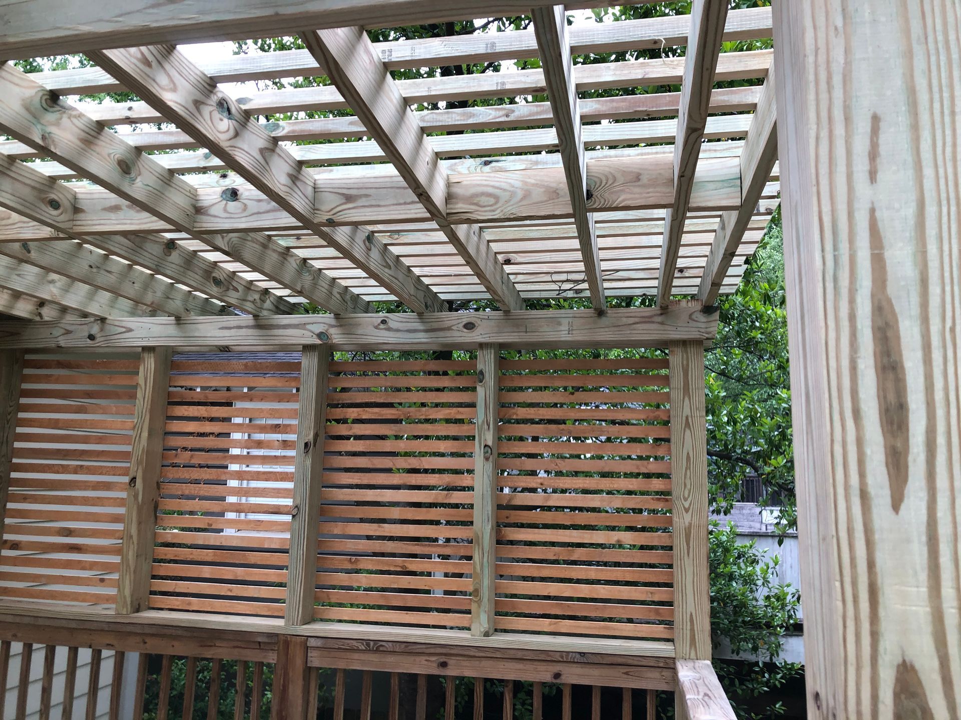 Wooden pergola with slatted walls and overhead beams in a garden setting