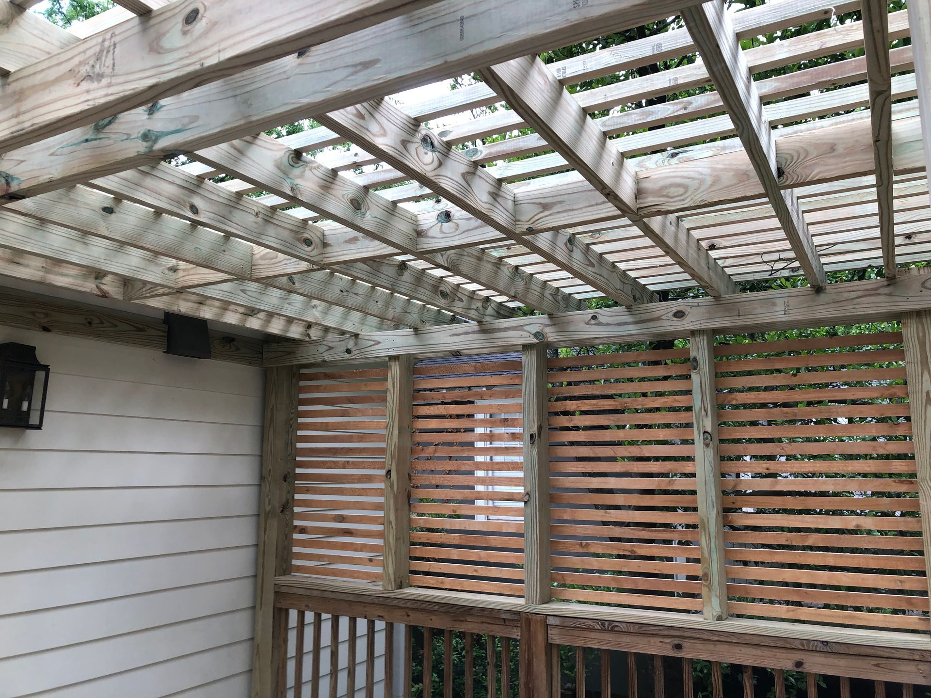 Covered outdoor patio with a weathered wooden lattice roof and slatted privacy wall