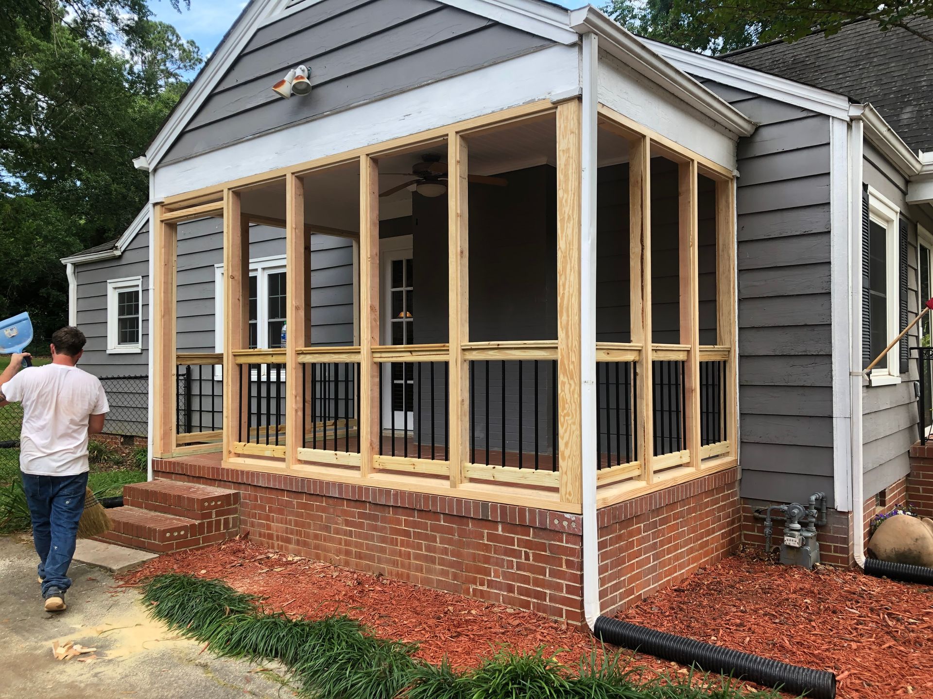 Person building a screened-in front porch on a gray house with brick steps and exposed framing