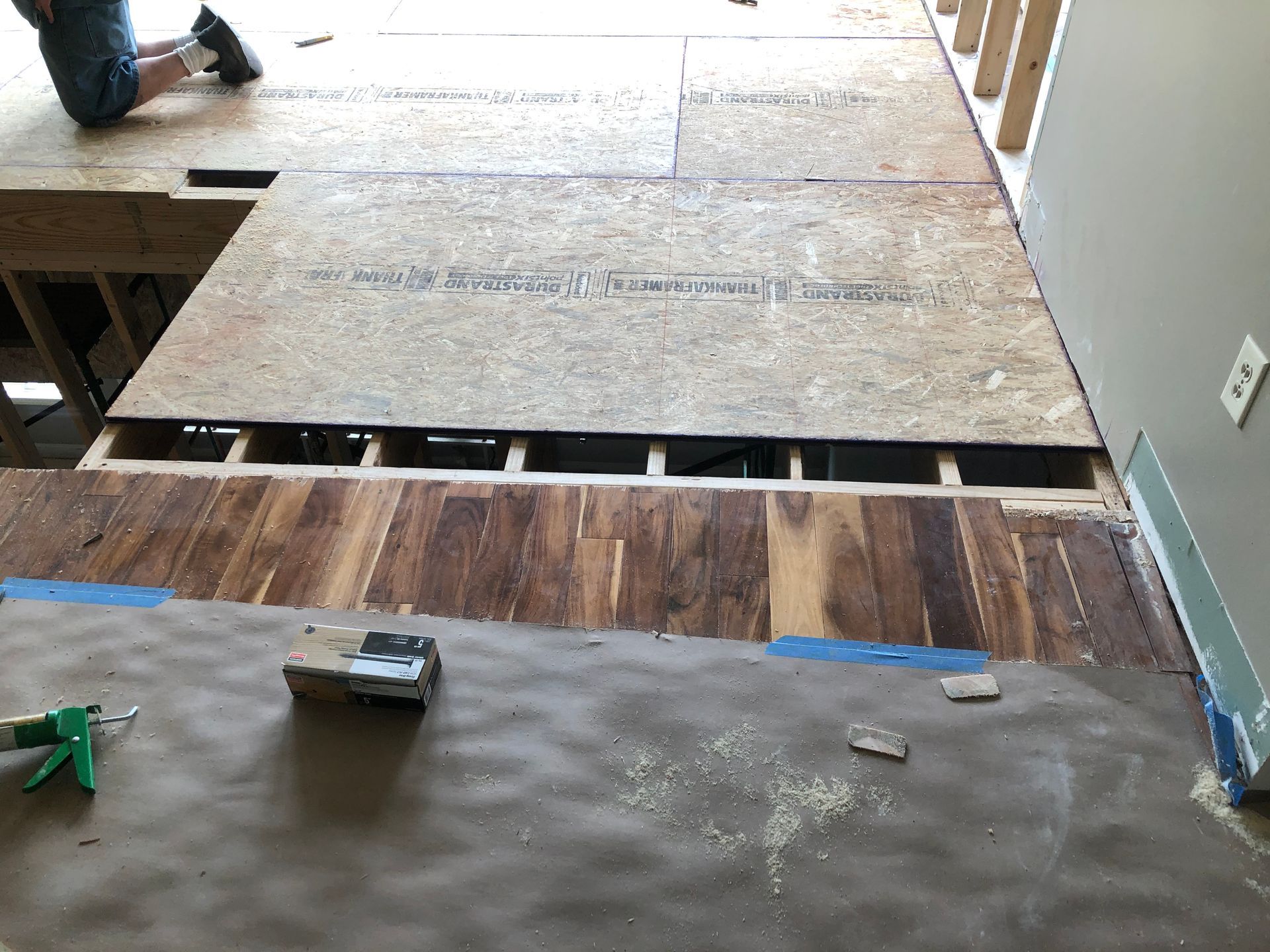 Construction floor with plywood sheets, exposed joists, and tools on a gray work surface