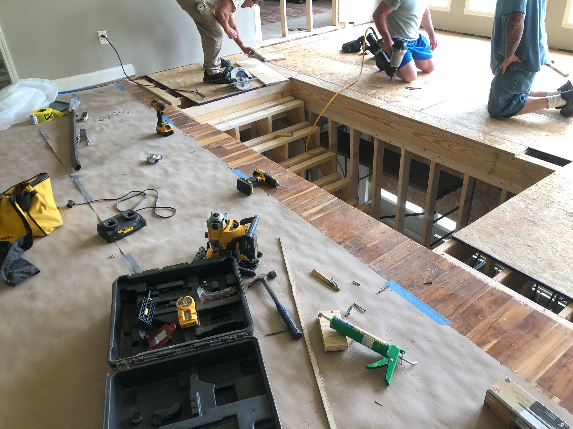 Workers installing floor joists in a house under construction, with tools and plywood sheets on the floor