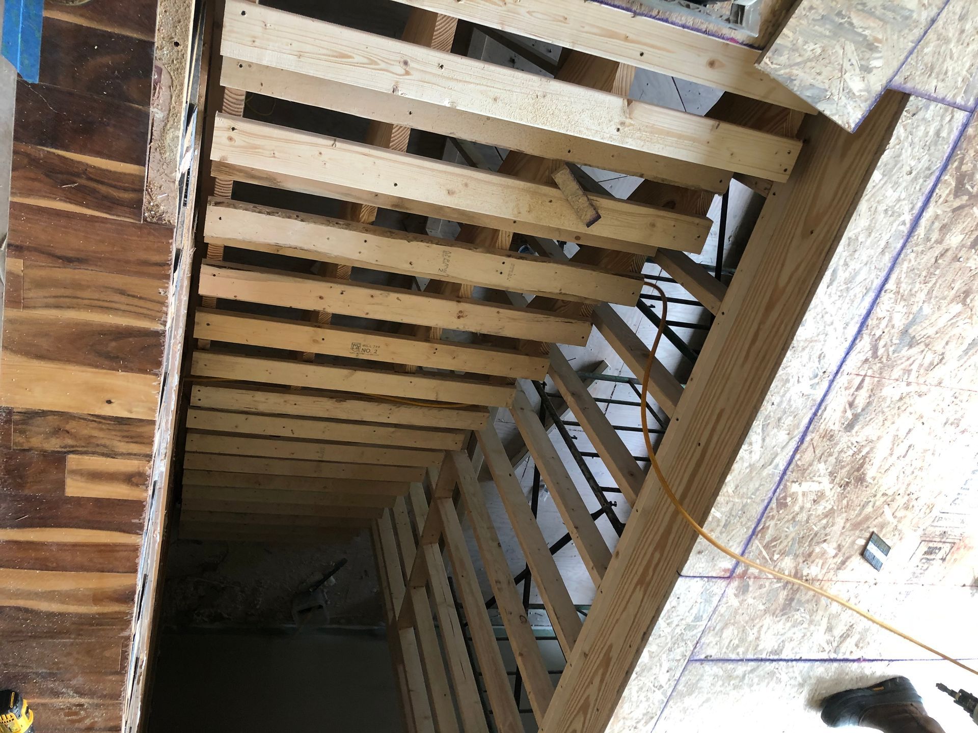 View looking down a narrow wooden stairwell with exposed joists and dark space below