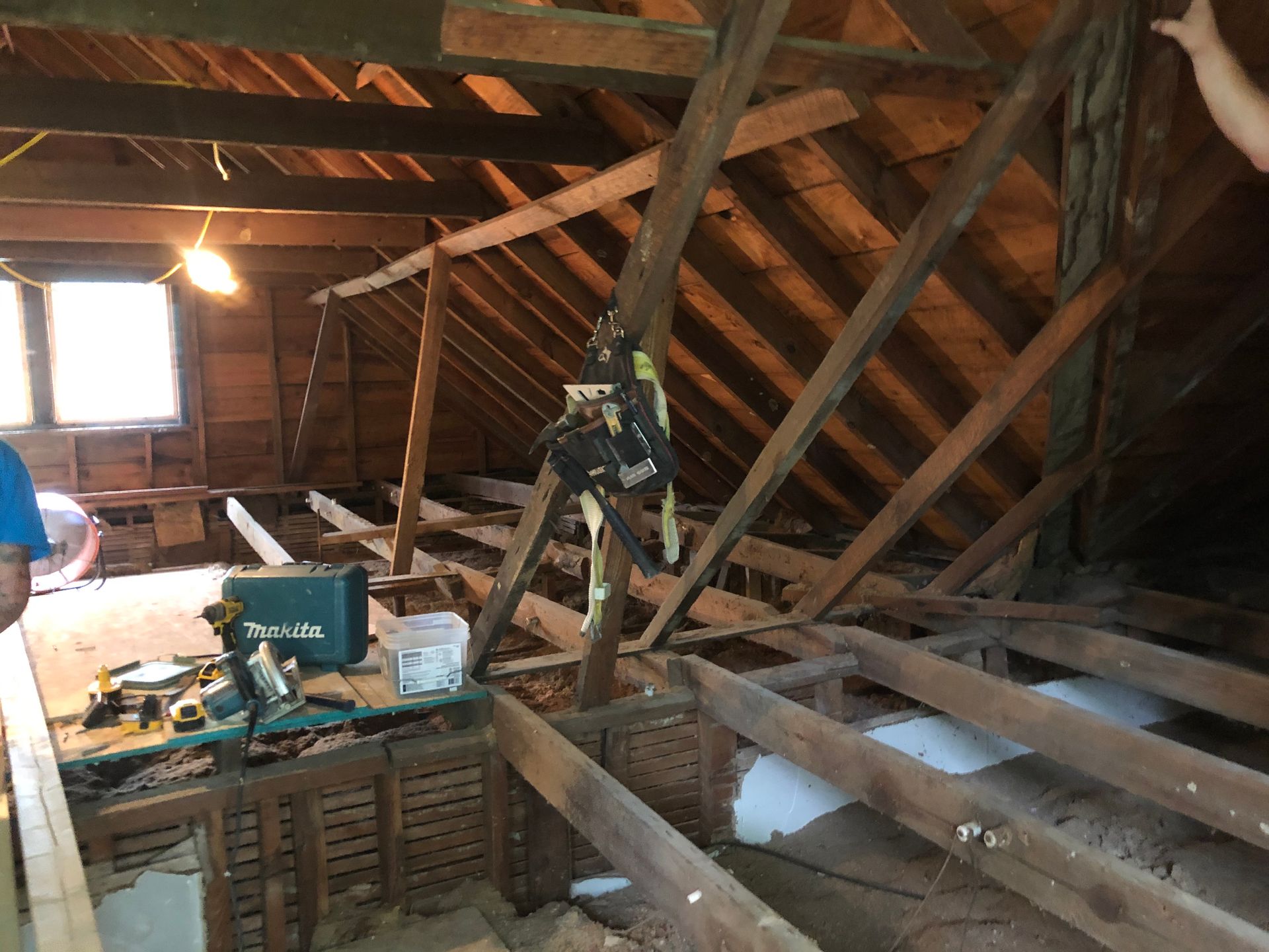 Attic with exposed wooden beams, a window, and scattered tools and lumber under a sloped roof.