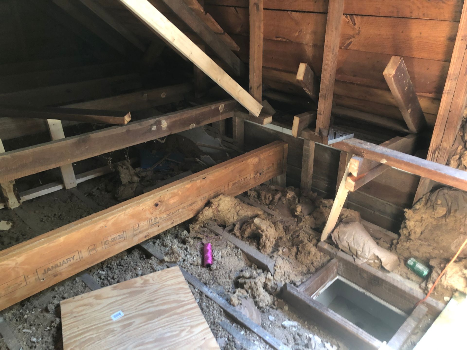 Damaged attic floor with exposed beams, insulation debris, and a window frame opening to below.