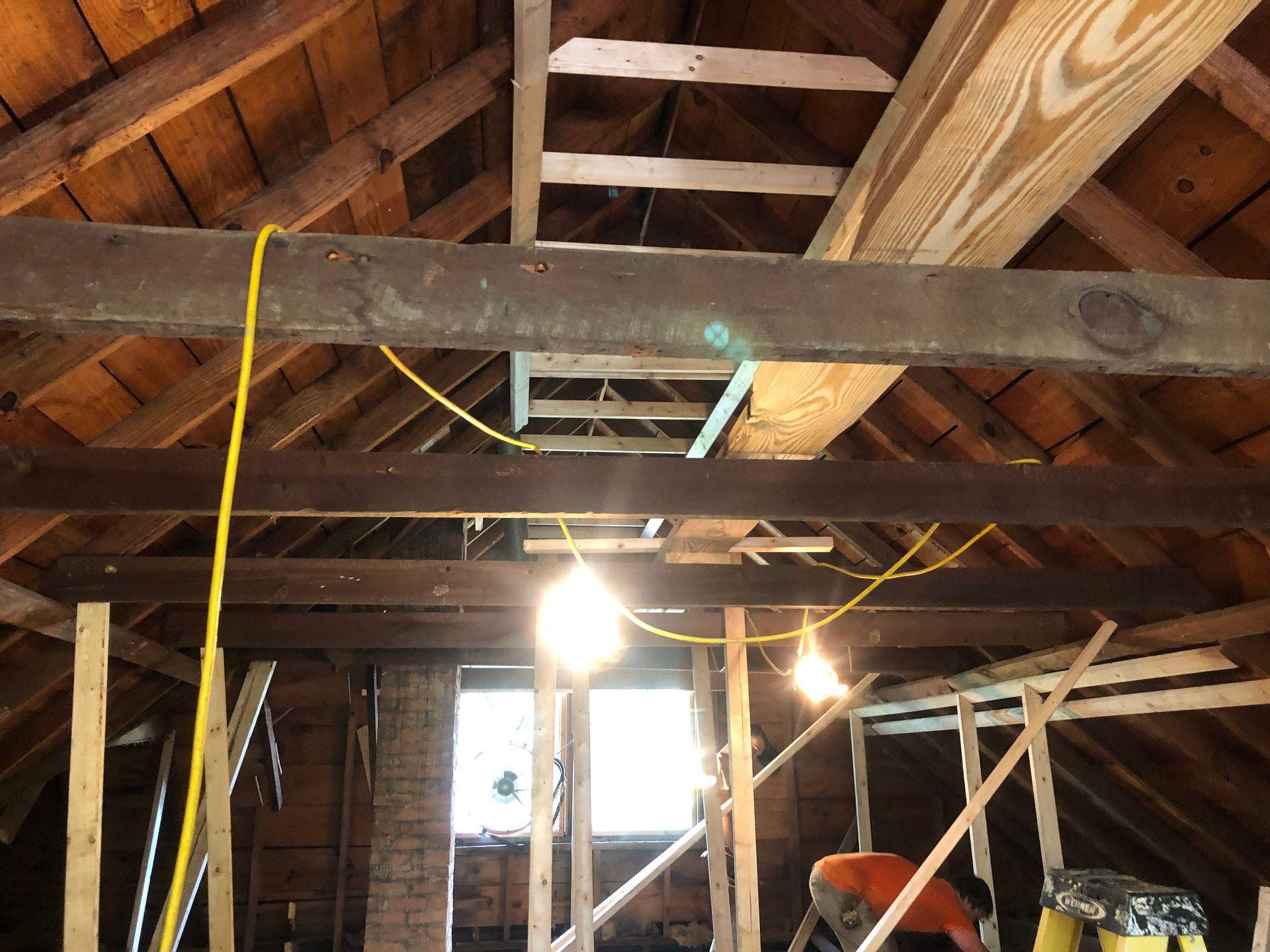 Exposed attic with wooden beams, hanging light bulbs, and loose electrical wiring during renovation