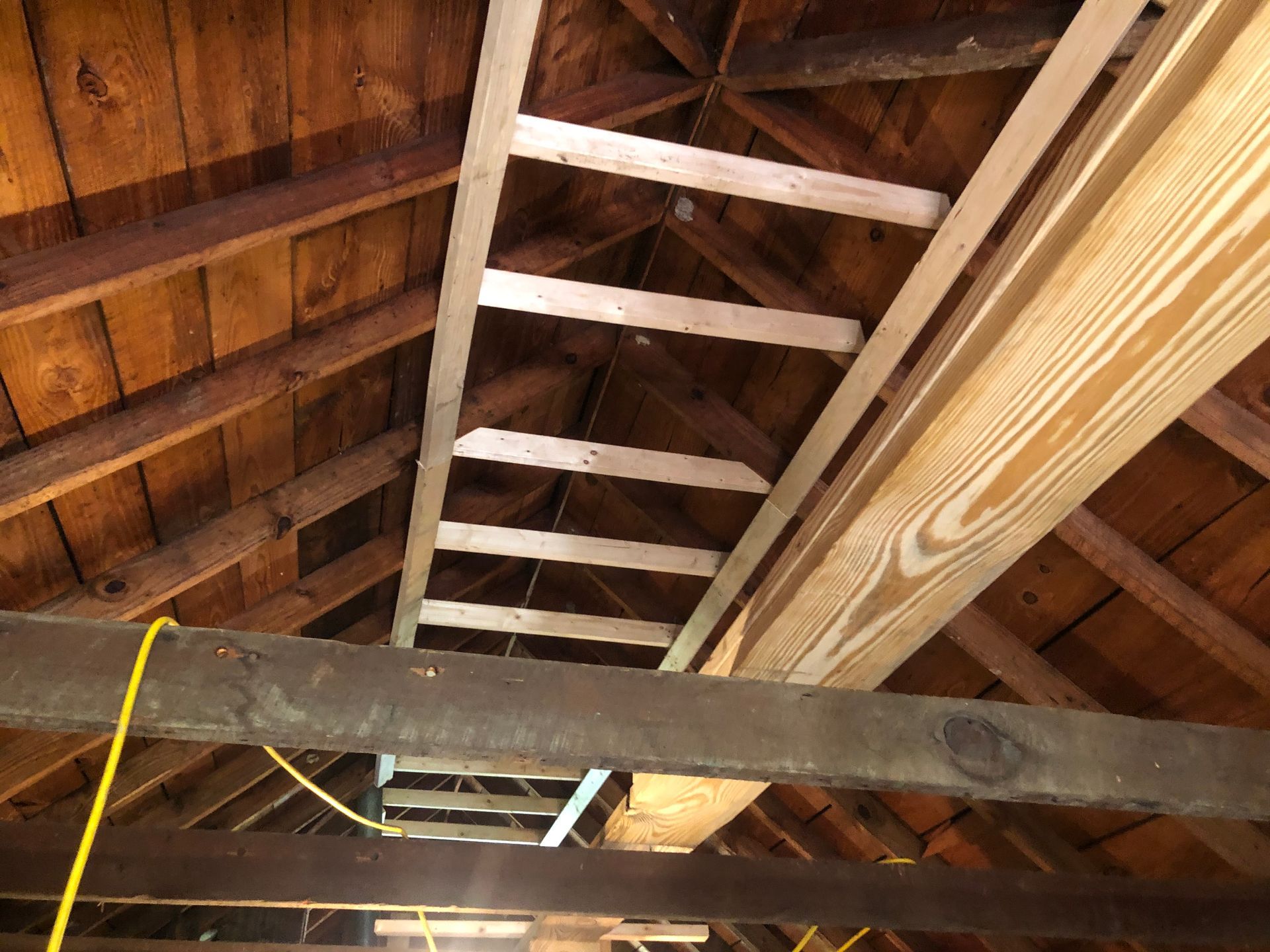 Wooden attic ceiling with exposed rafters and beams, viewed upward from below.