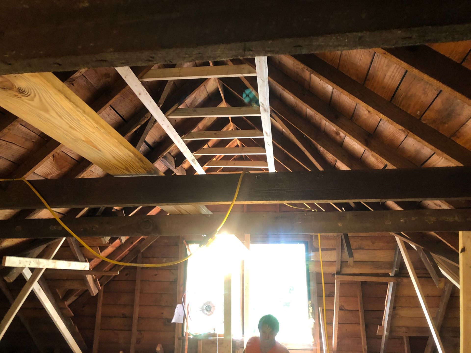 Attic interior with exposed wooden rafters and bright sunlight through a window, person standing below