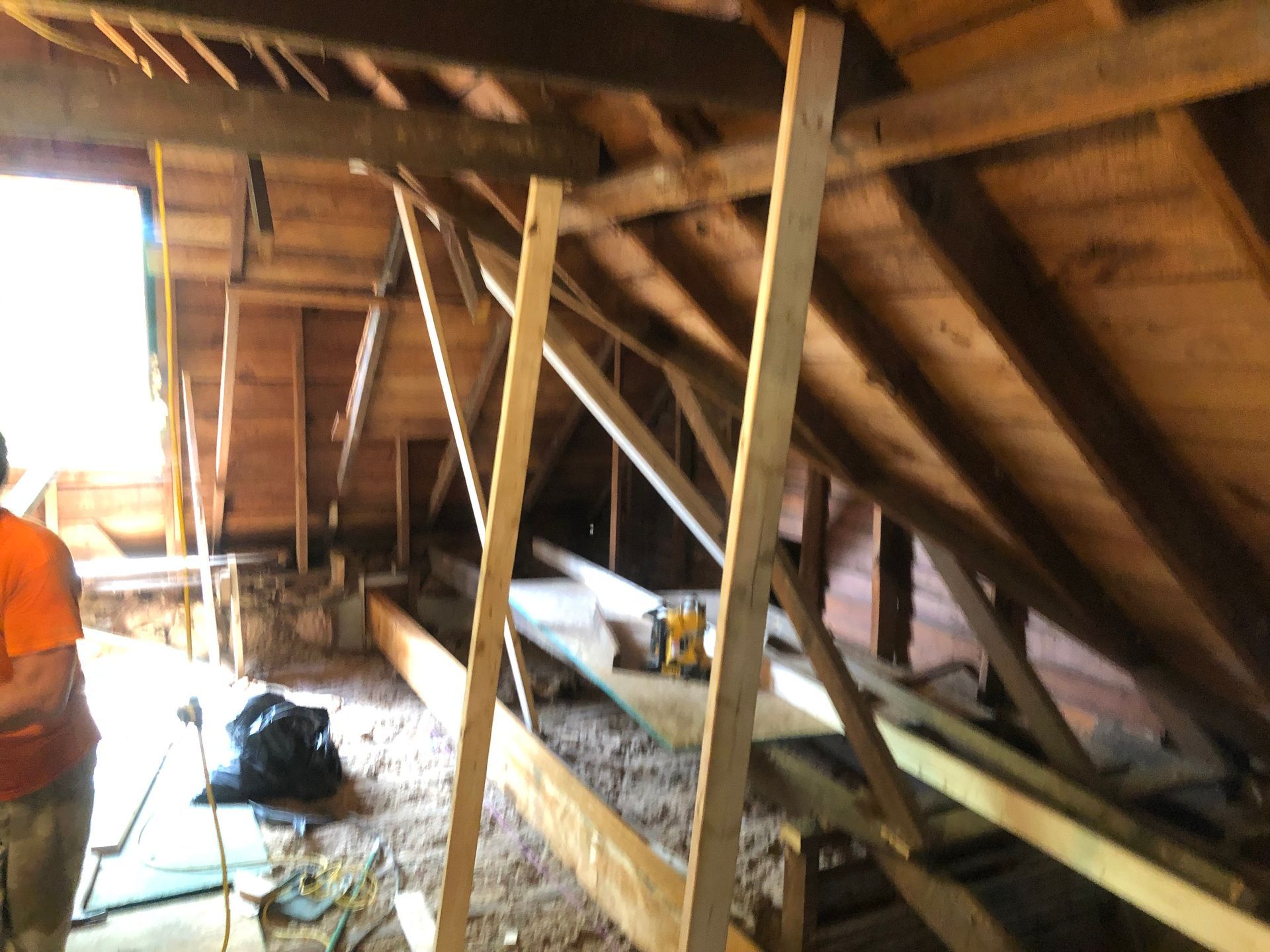 Attic interior with exposed wooden beams, roof braces, and scattered tools and materials on the floor