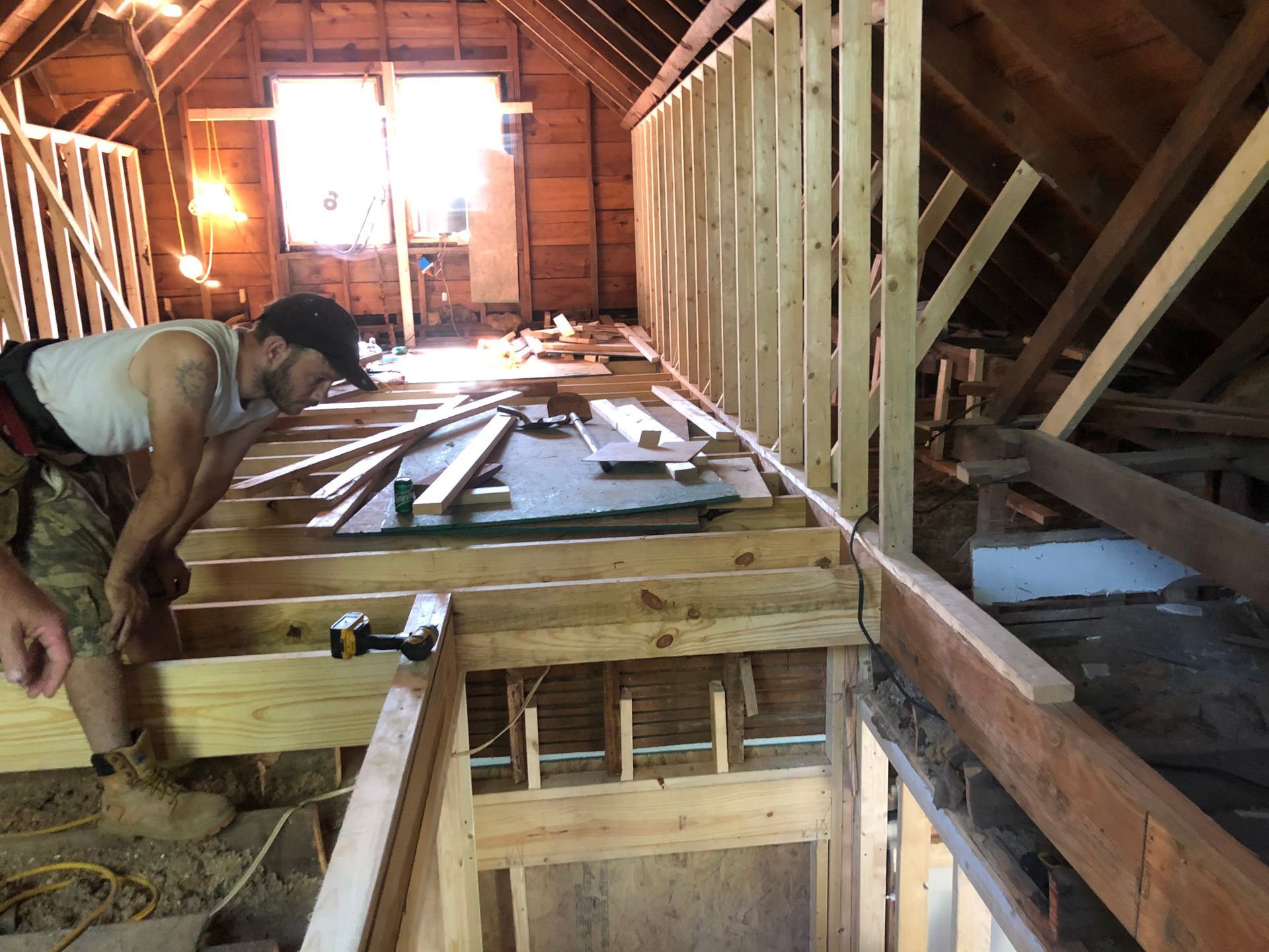 Worker framing a wooden attic interior with exposed beams and tools on the floor