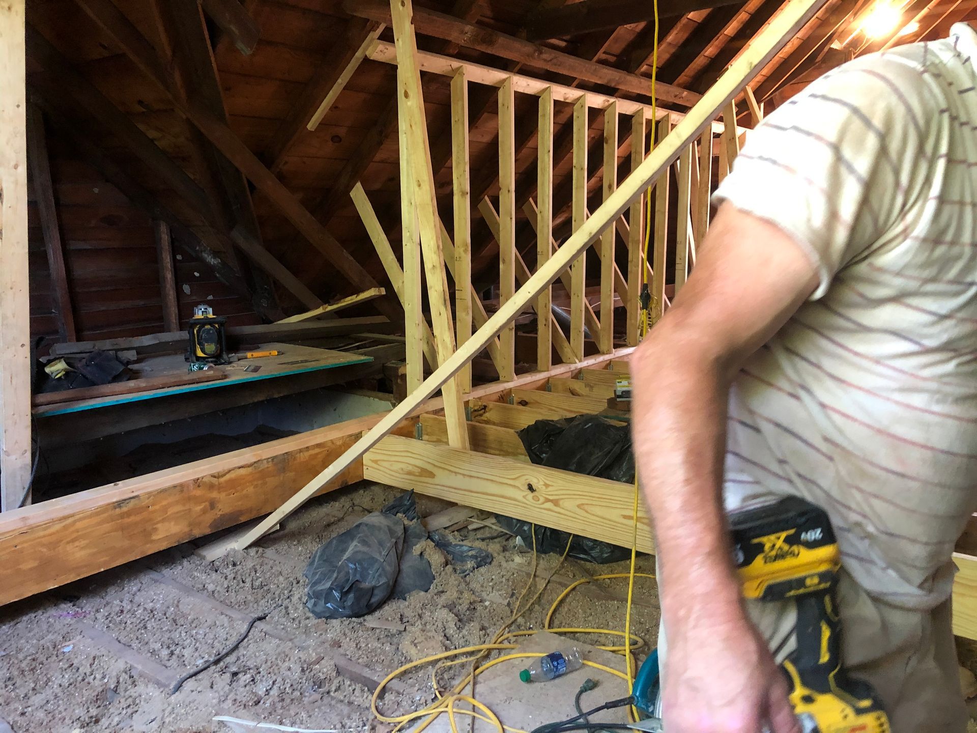 Person in striped shirt working with a power tool in an attic under construction