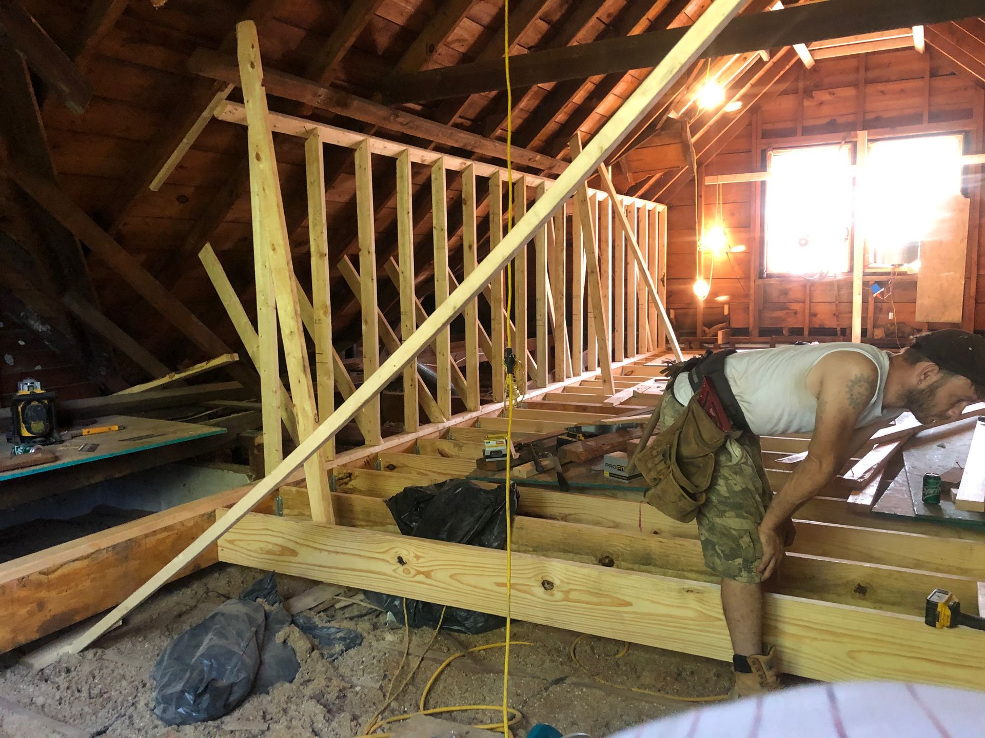 Man framing a wall inside an attic with exposed beams and bright sunlight through windows