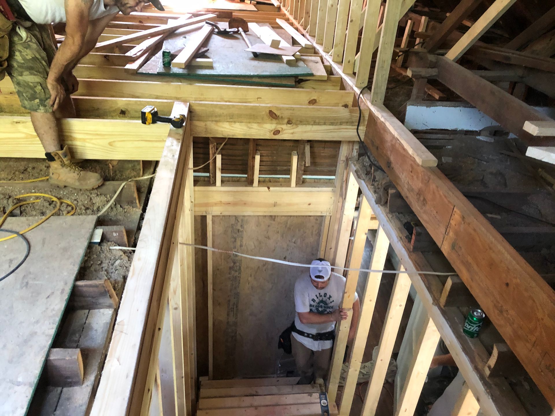 Interior of a house under construction, showing wooden framing and a stairwell opening.