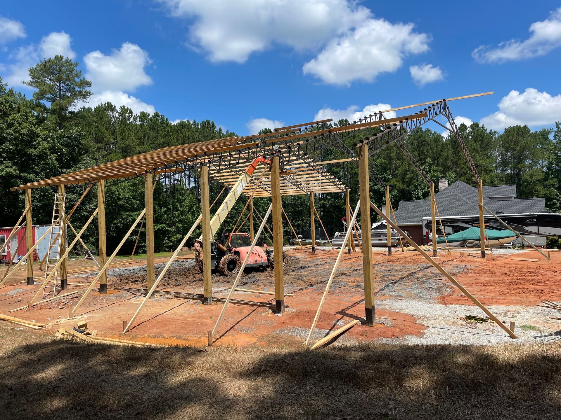 Partially built wooden structure on a dirt lot with a tractor and scattered construction materials under blue sky