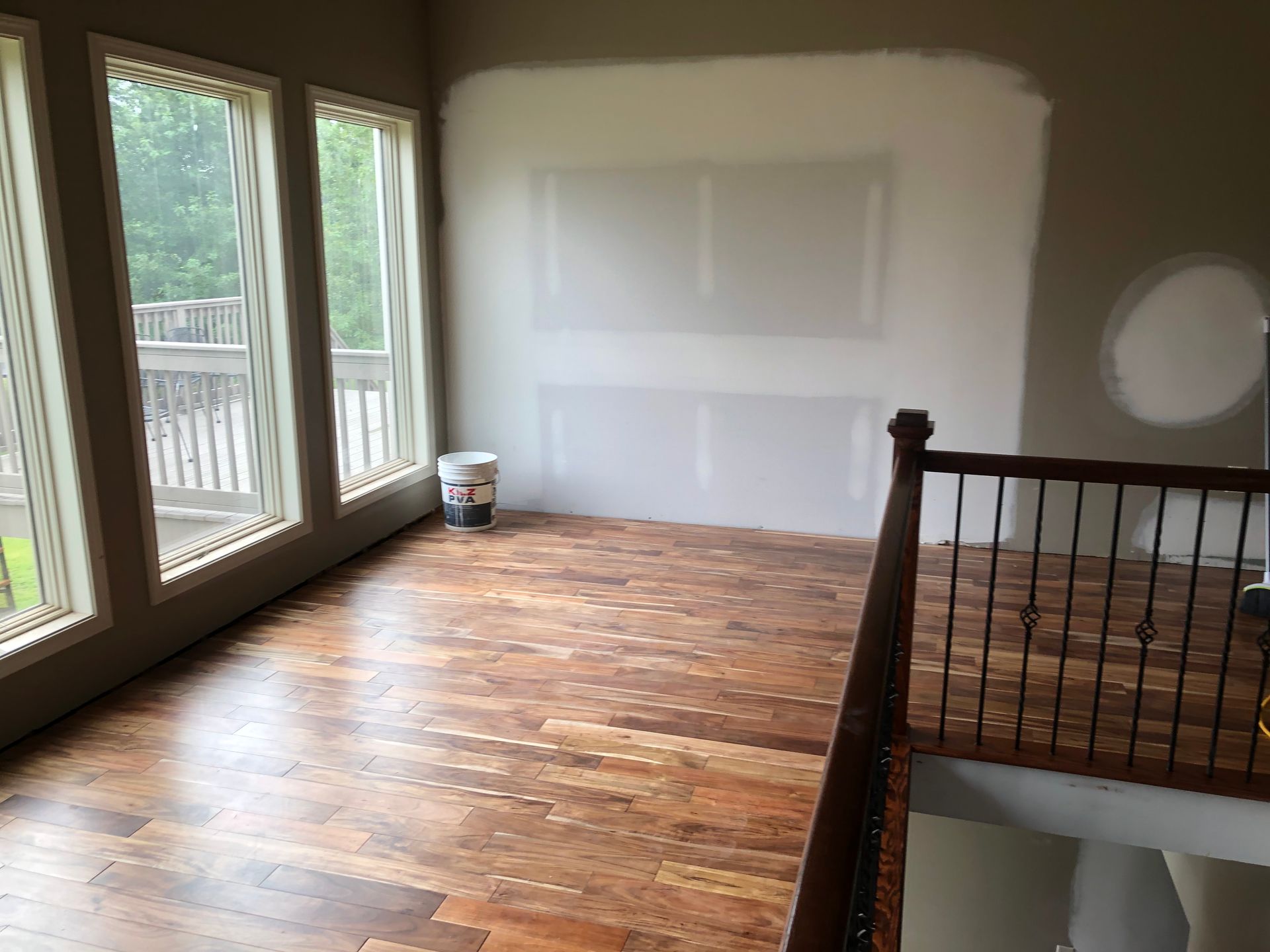 Empty room with hardwood floors, large windows, and a white-painted wall near a stair railing
