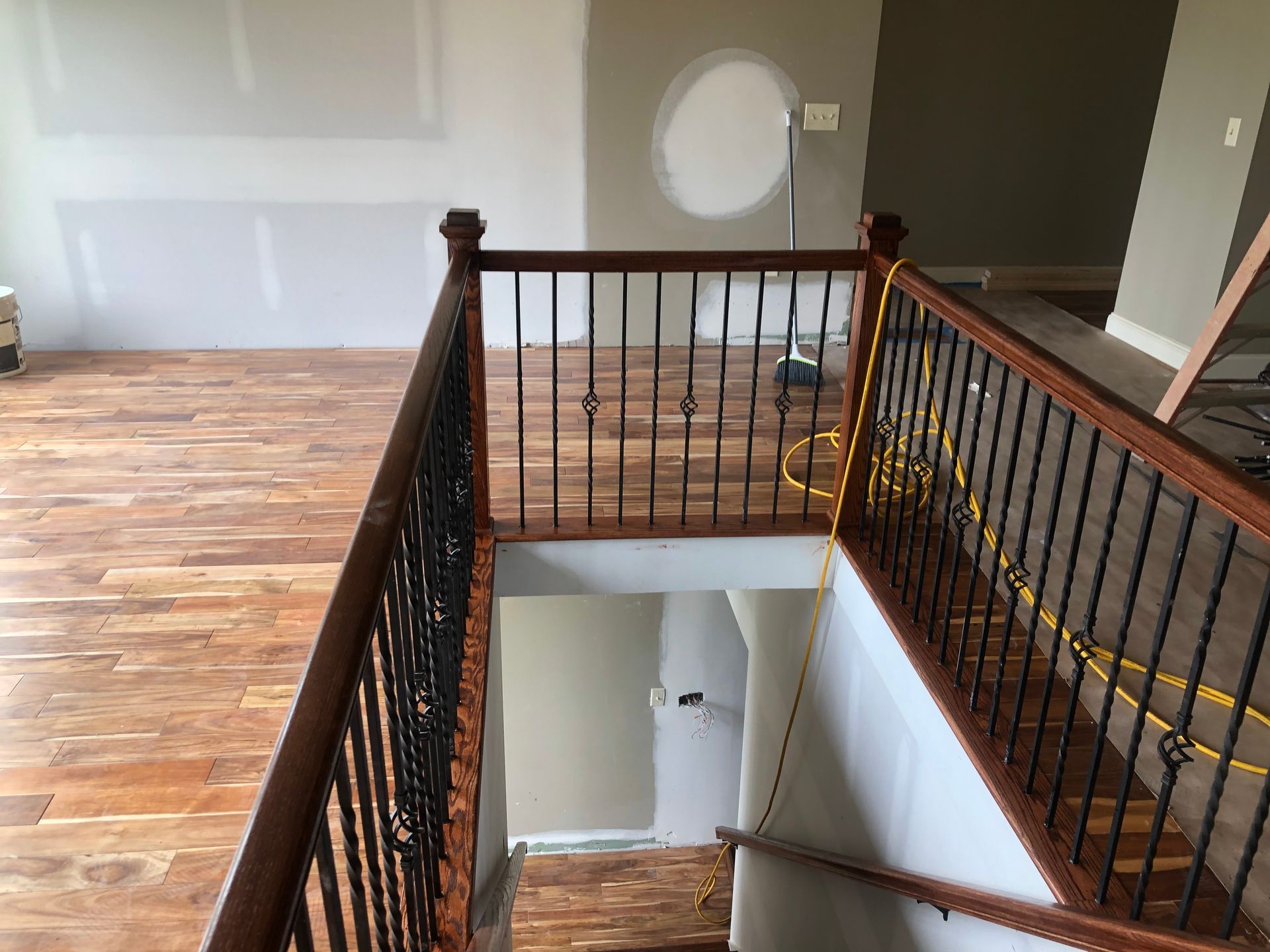 Interior balcony overlooking staircase with black railing, hardwood floor, and round mirror on the wall