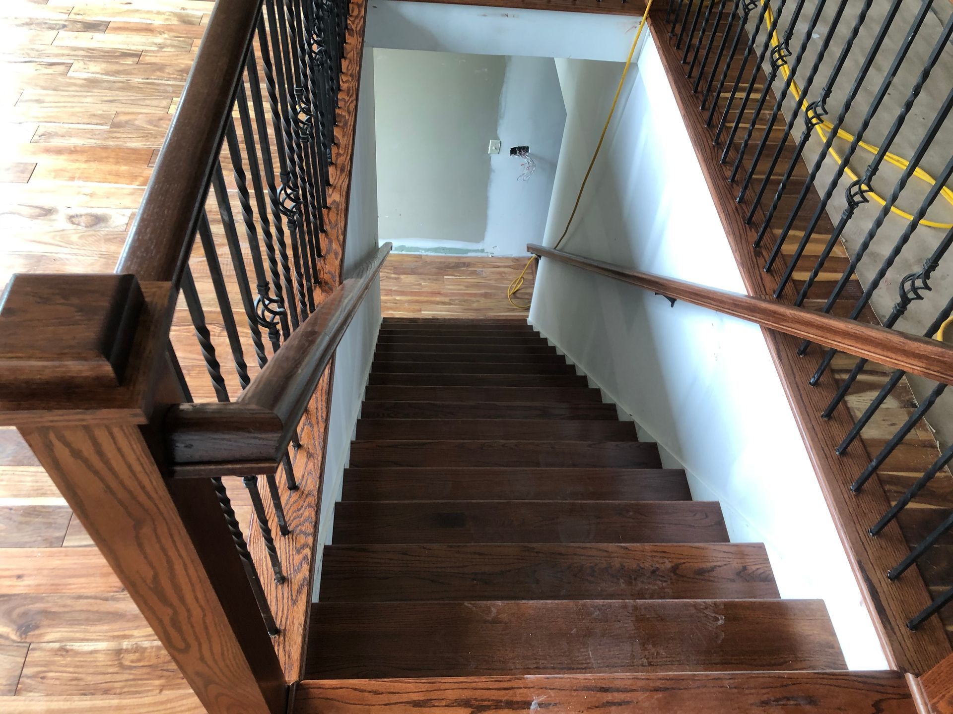 Wooden staircase with dark steps and black railings descending into a hallway