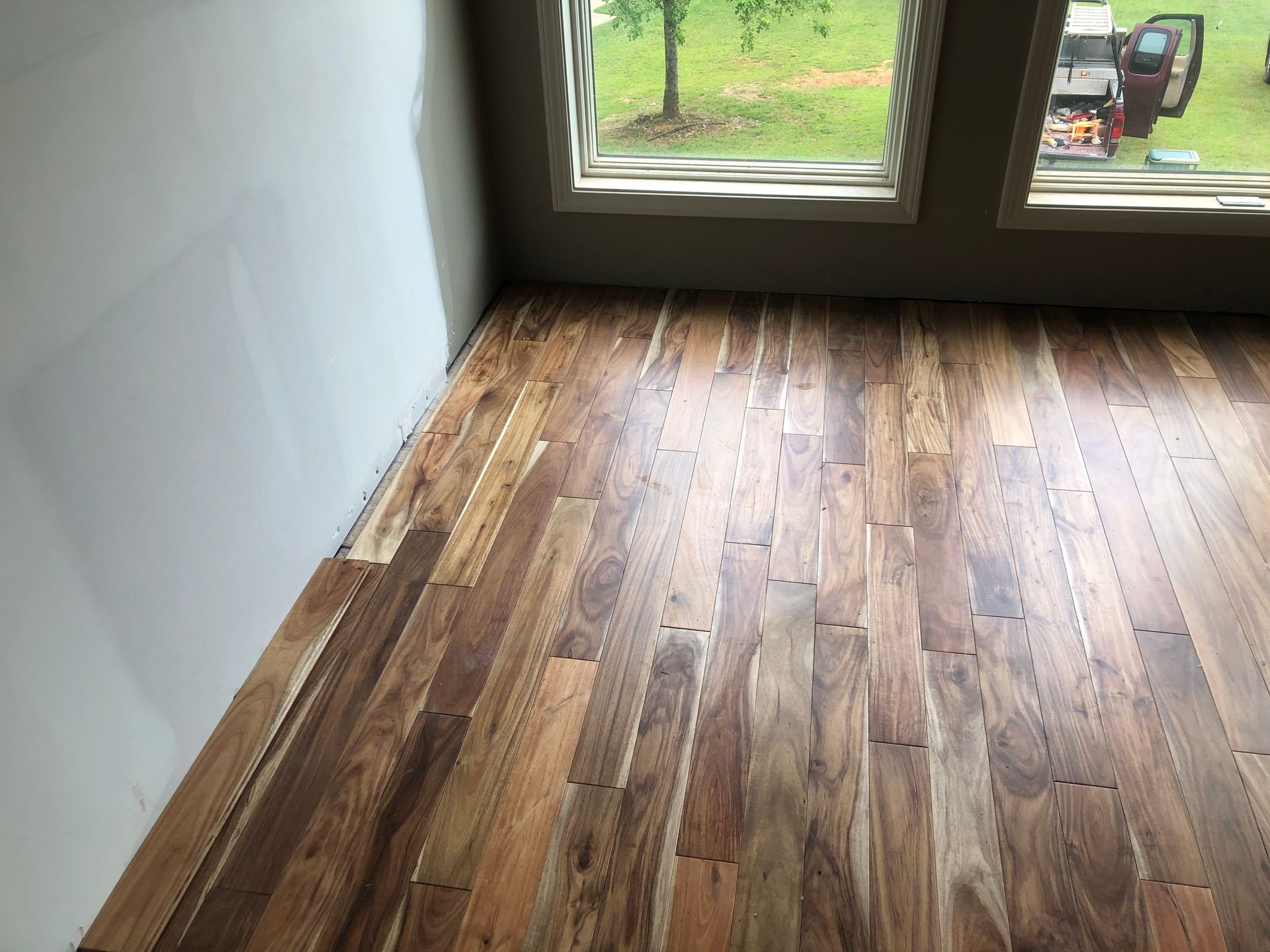 Empty room with wood plank floor and large windows overlooking a grassy yard