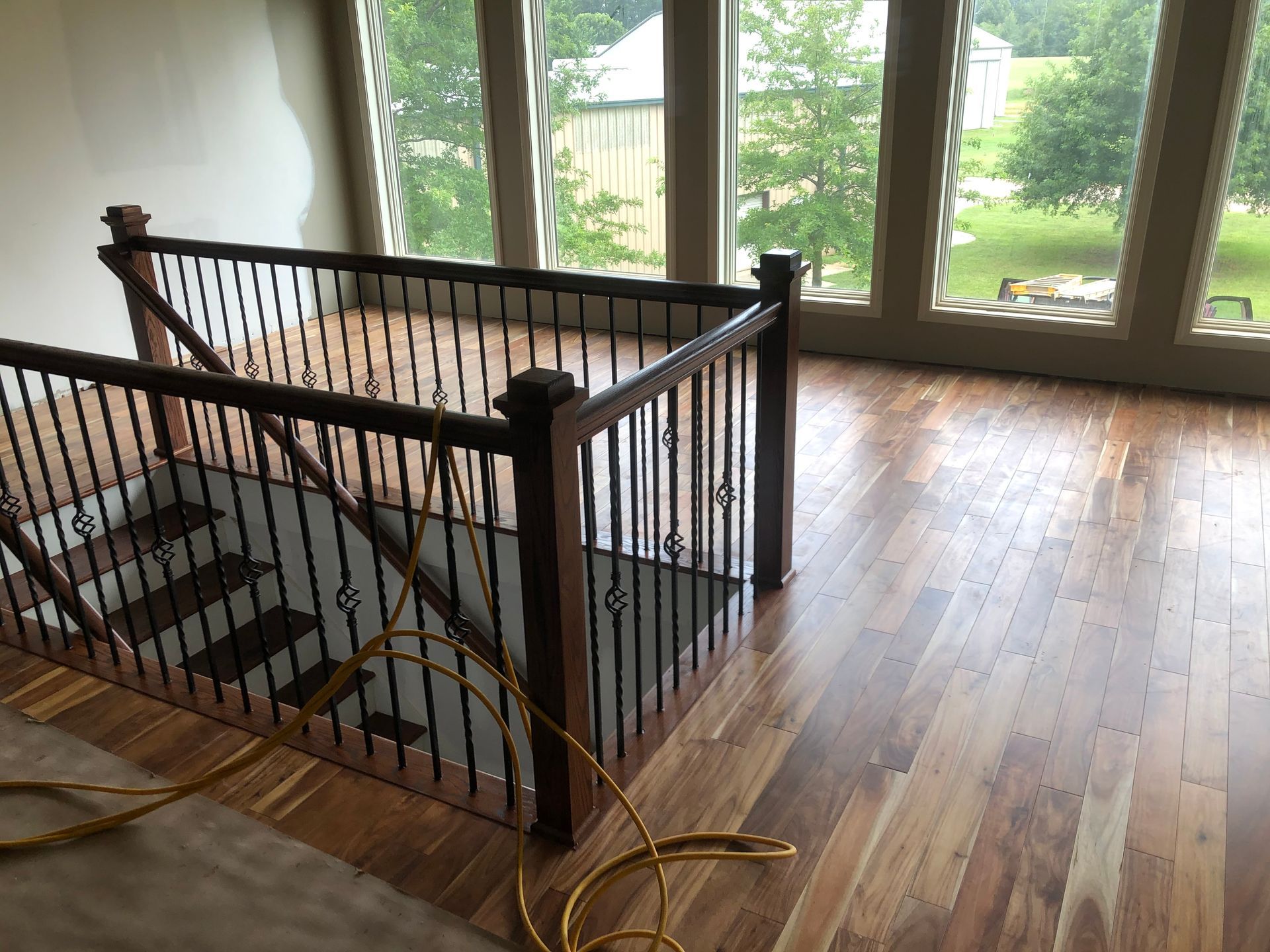 Stairwell with black railing and wood floors beside large windows, with a cord on the floor