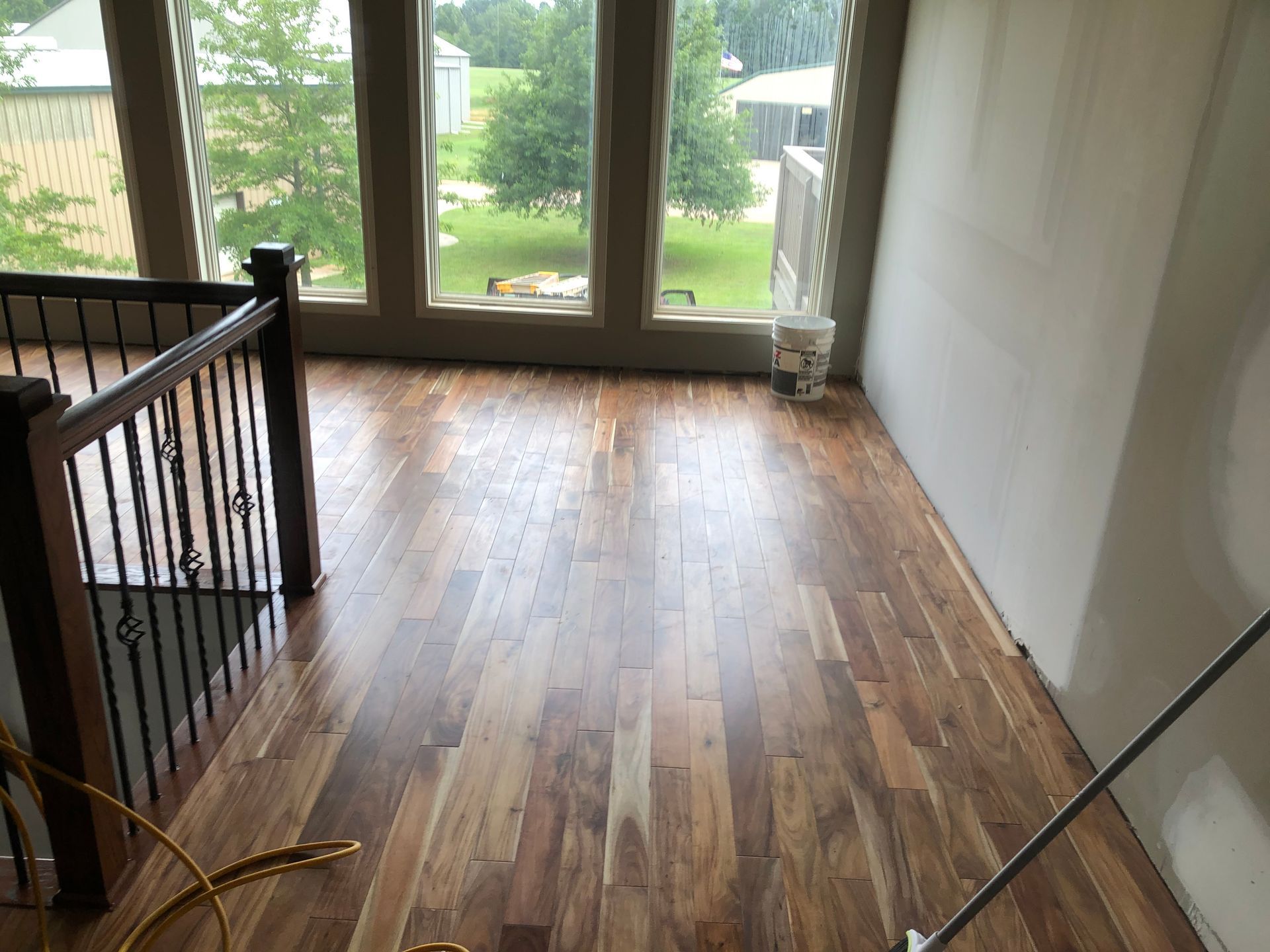 Empty hardwood room with large windows, stairs on left, and a coiled hose on the floor