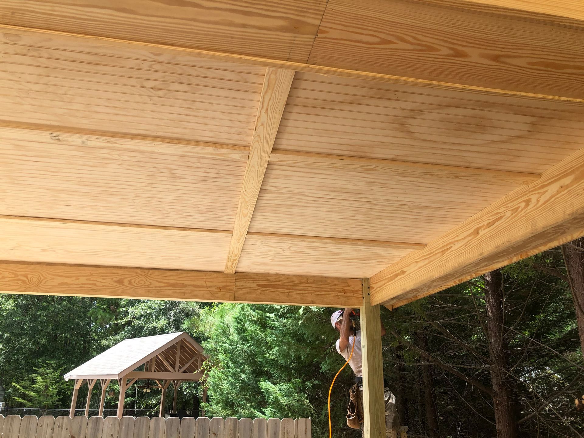 Wooden gazebo roof under construction, with trees and a small shed in the background.