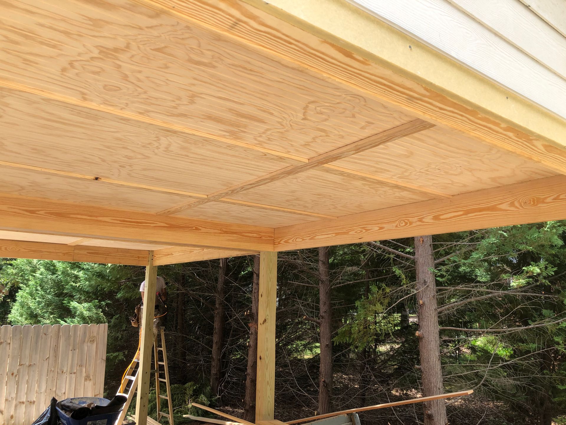 Wooden deck under construction with exposed joists and support posts beside a wooded yard