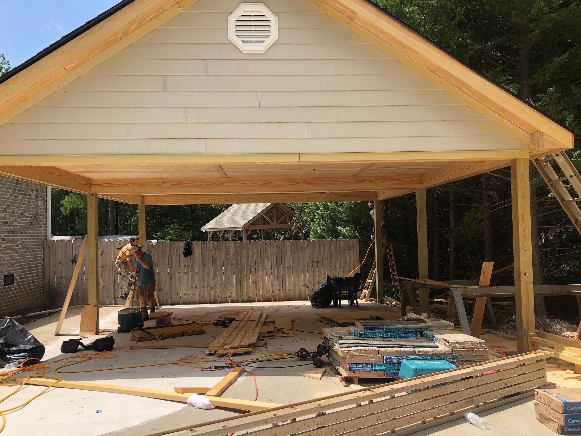 Partially built wooden carport with a gabled roof and construction materials scattered underneath