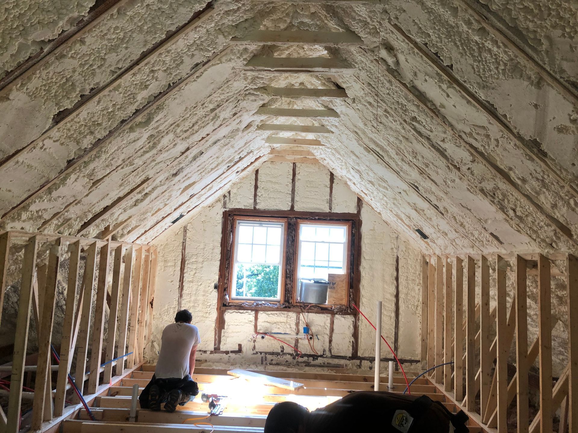 Attic under renovation with exposed rafters, insulation, and a worker near a window at the far end