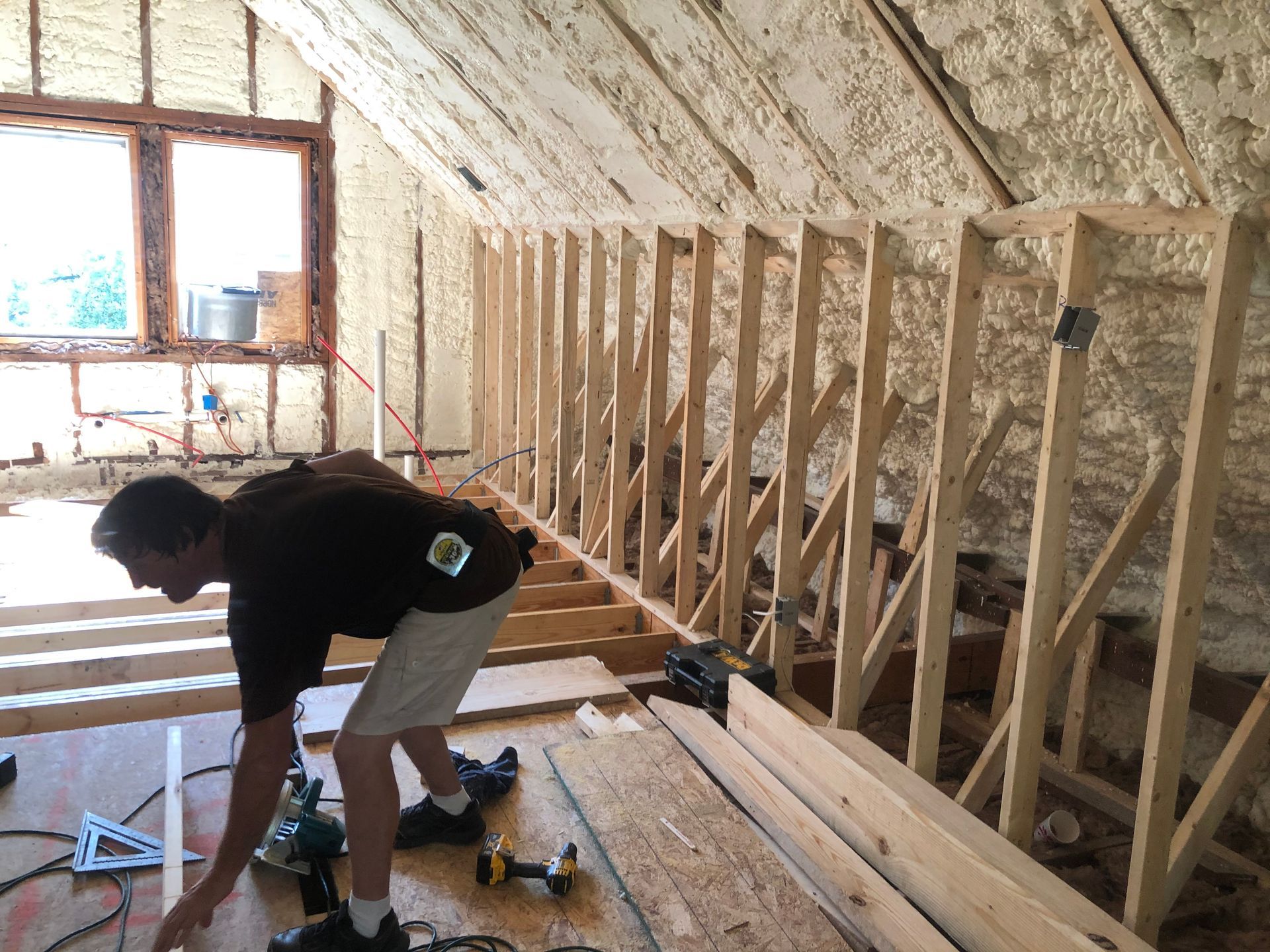 Worker installing floor joists in an unfinished attic with exposed insulation and wooden framing