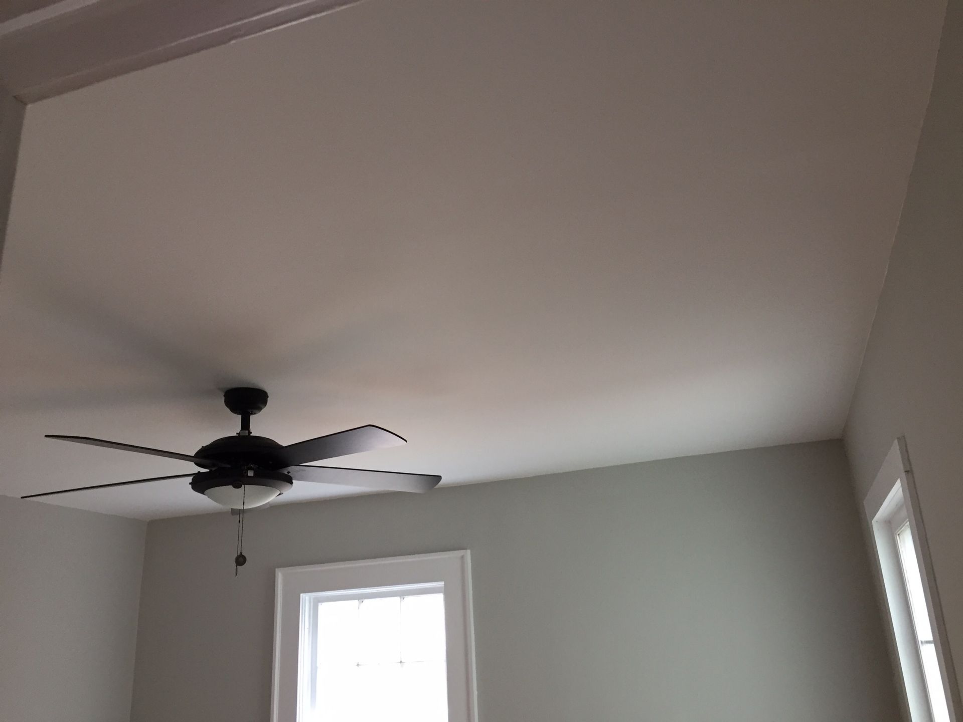 Ceiling fan in a white room with two windows and a slanted ceiling.
