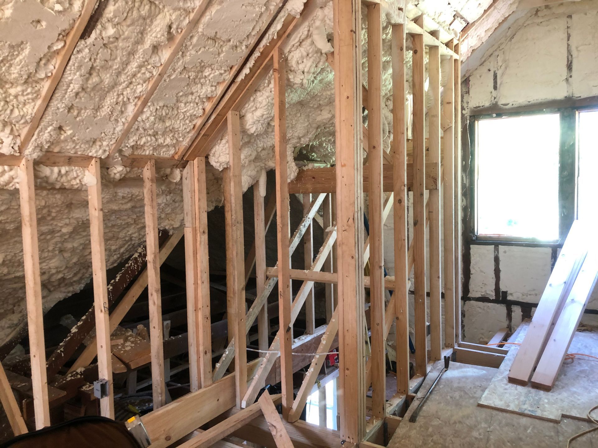 Attic under renovation with exposed wood framing, insulation, and stacked boards near a window
