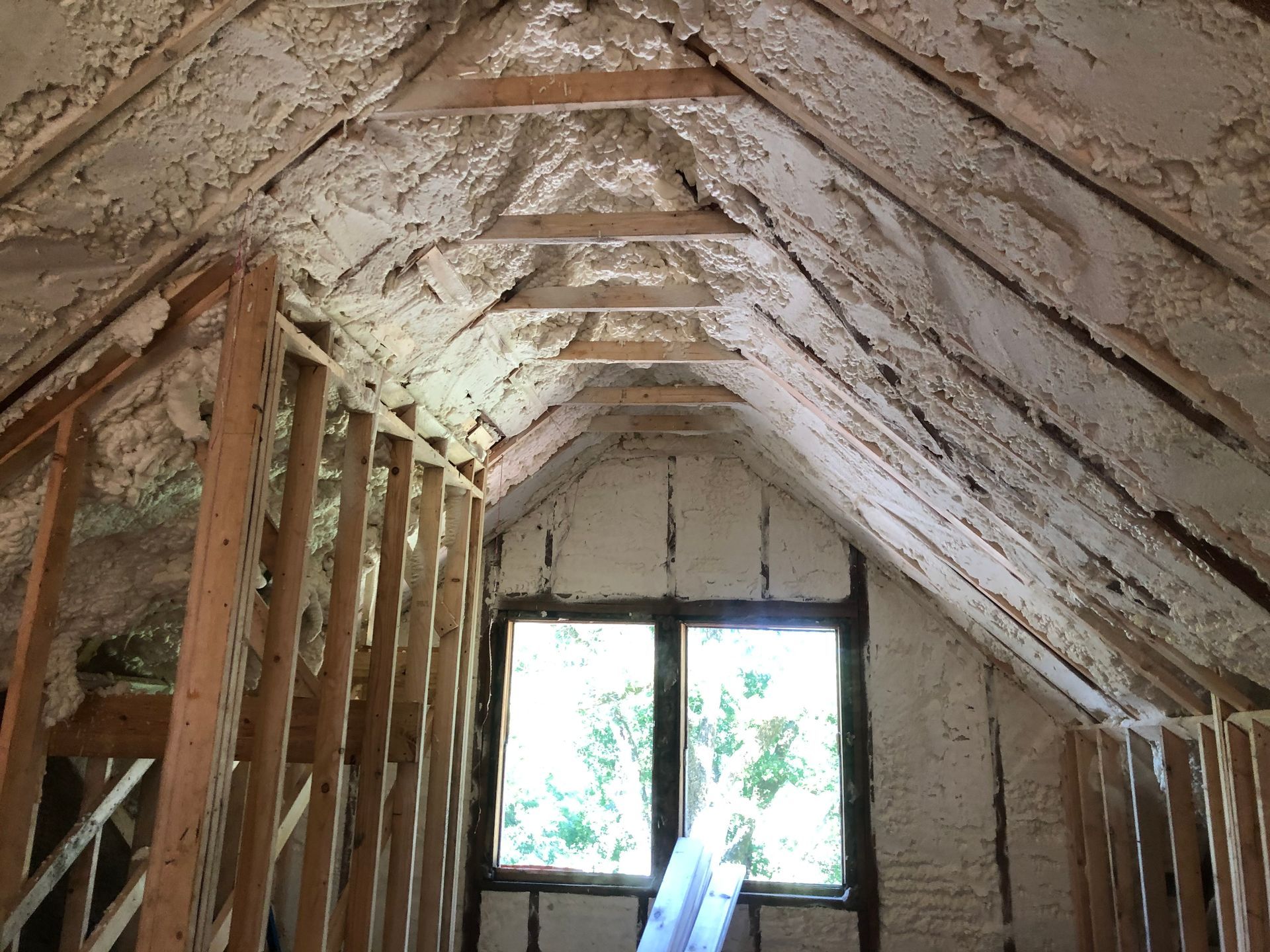 Attic interior with exposed roof rafters, insulation, and a window at the far end.