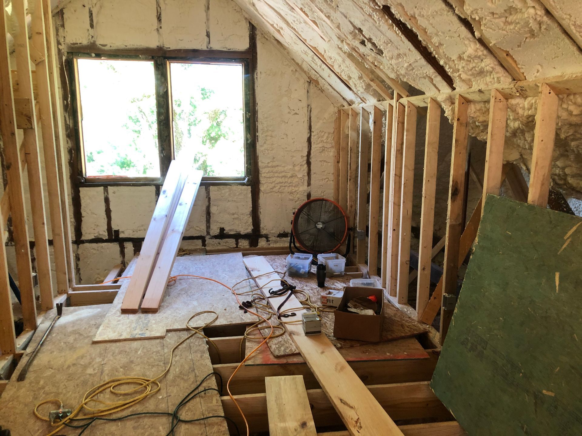 Unfinished attic with exposed rafters, window light, insulation, and tools scattered on the floor during renovation