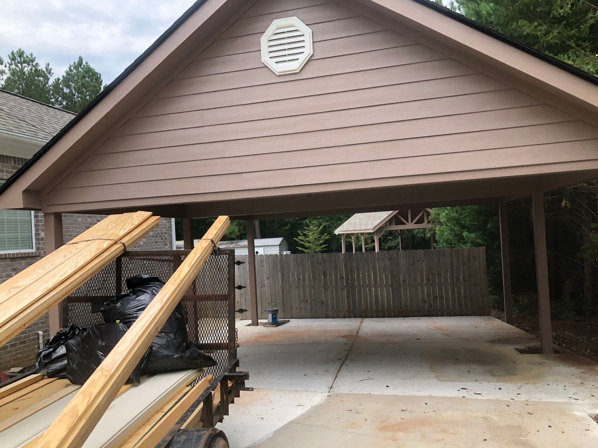 Brown carport attached to a house, with wooden ramps and a concrete driveway underneath.