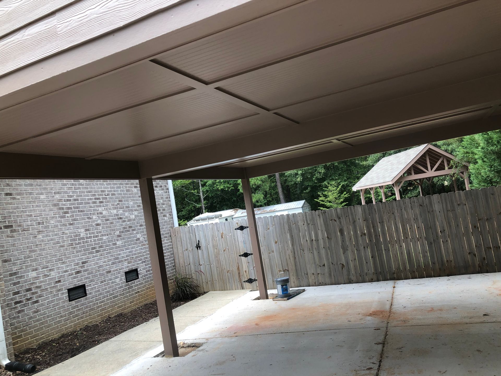 Covered patio with concrete floor, wooden posts, white brick wall, and fenced backyard beyond.