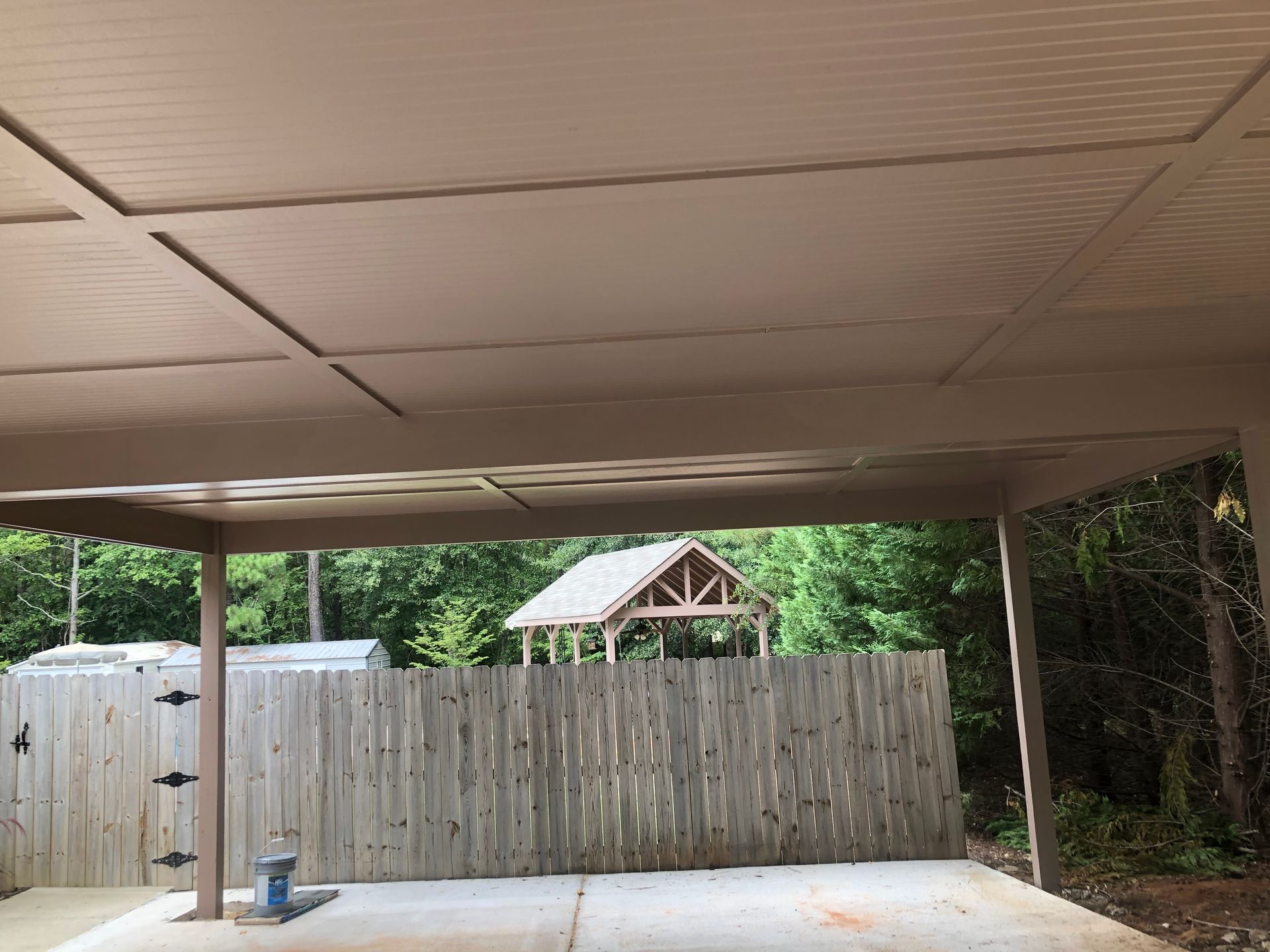 Covered patio facing a wooden privacy fence with trees and a small gazebo beyond it