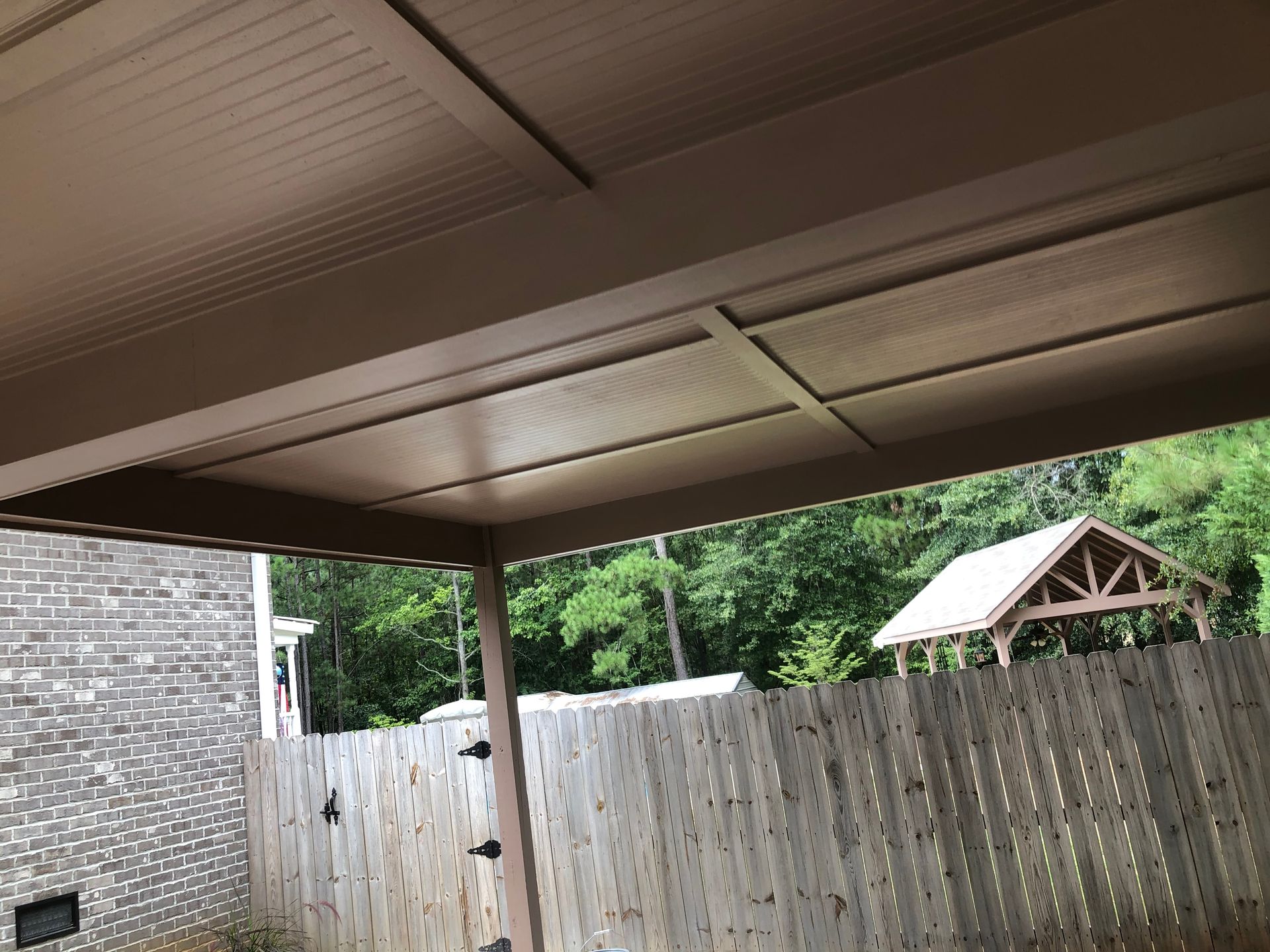 Covered patio with brown roof beams, stone wall, and a wooden privacy fence.