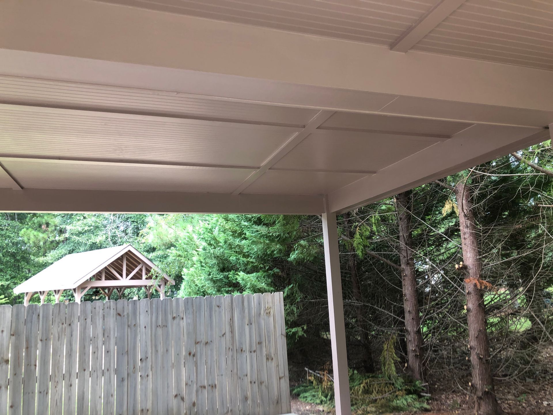 Porch overlooking a wooden fence, shed roof, and green trees in a backyard.