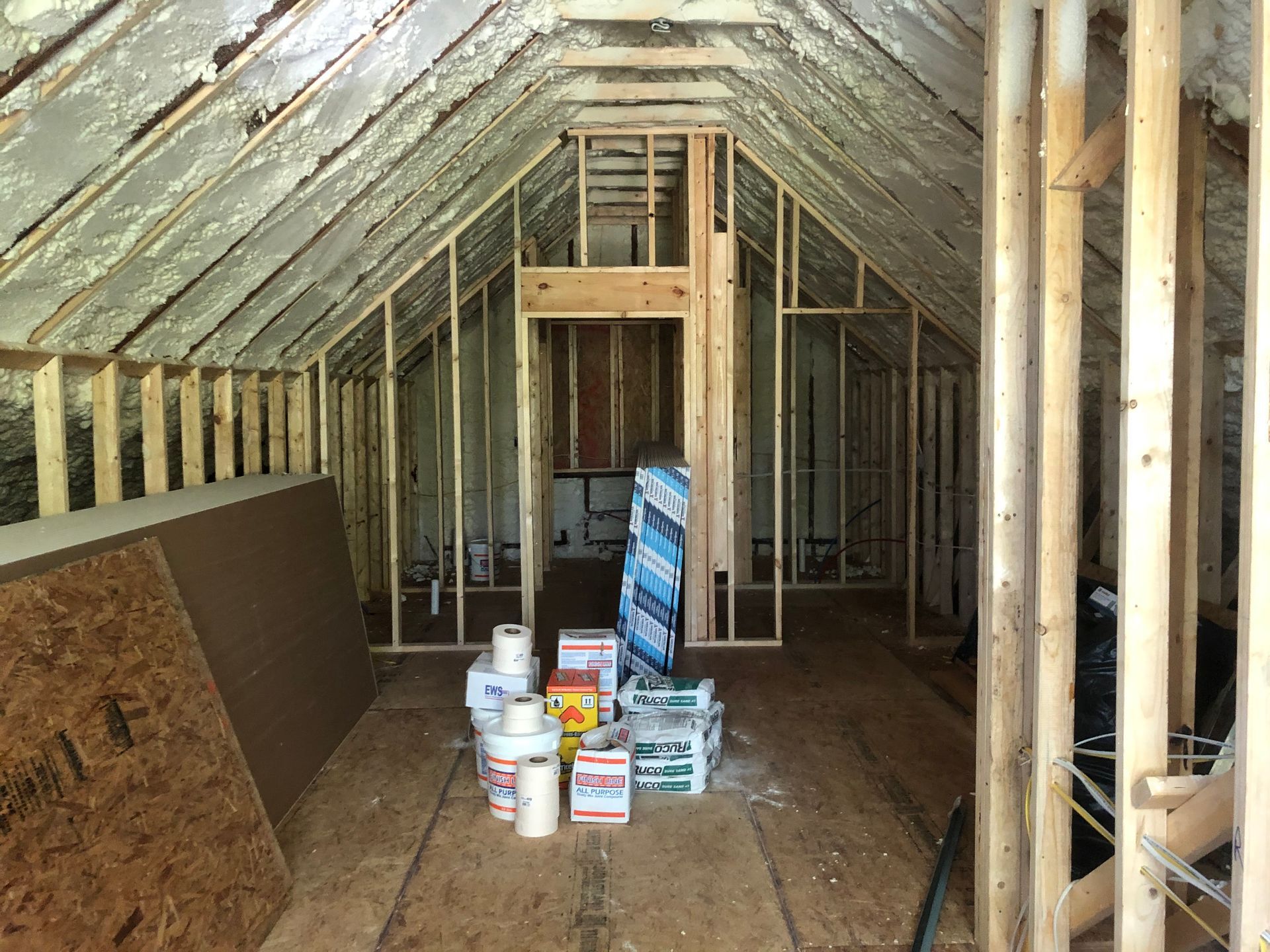 Unfinished attic framed with exposed rafters, plywood walls, and paint cans on the floor.