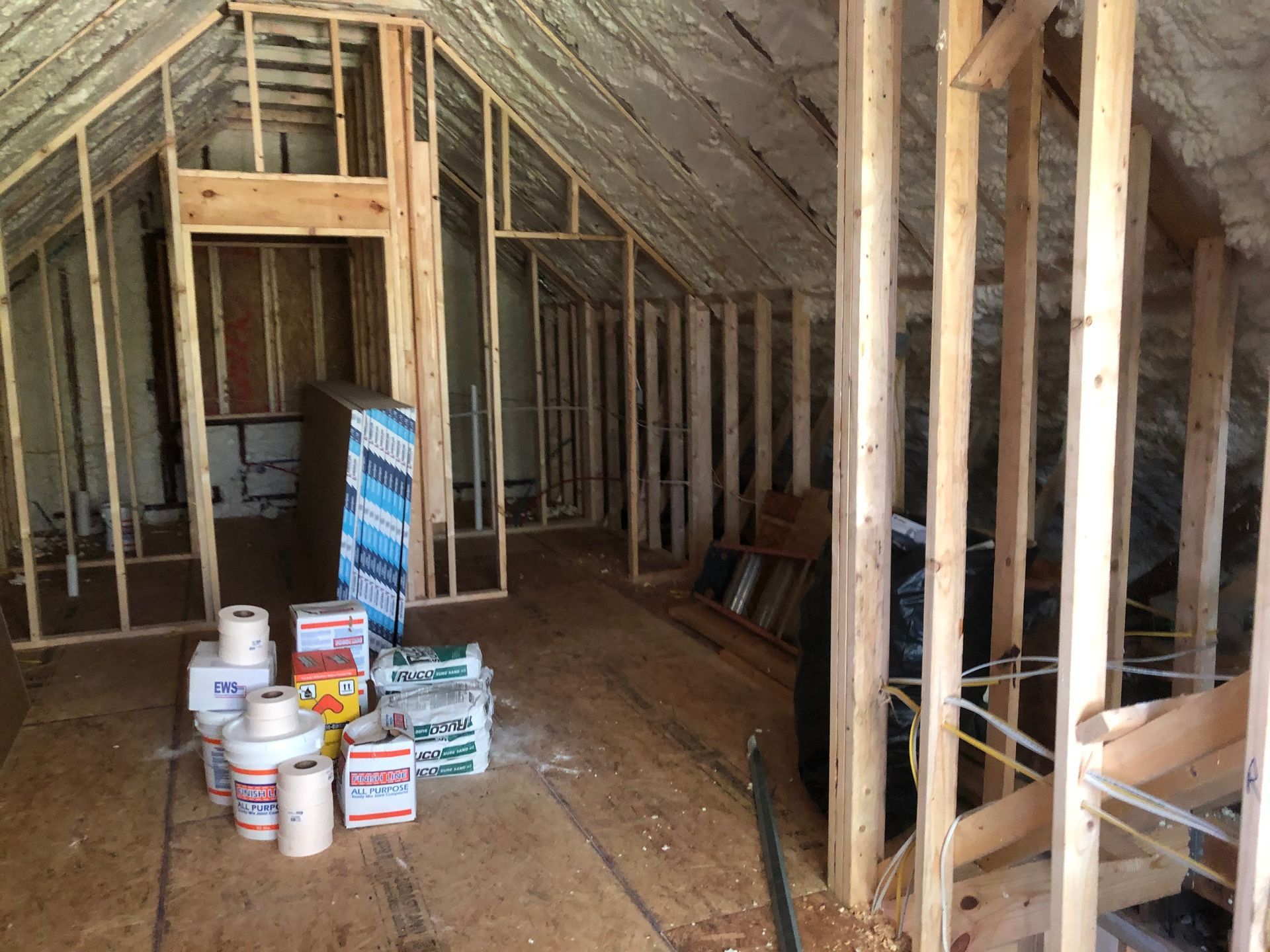 Attic under construction with exposed studs, stacked paint cans, and building materials on the floor