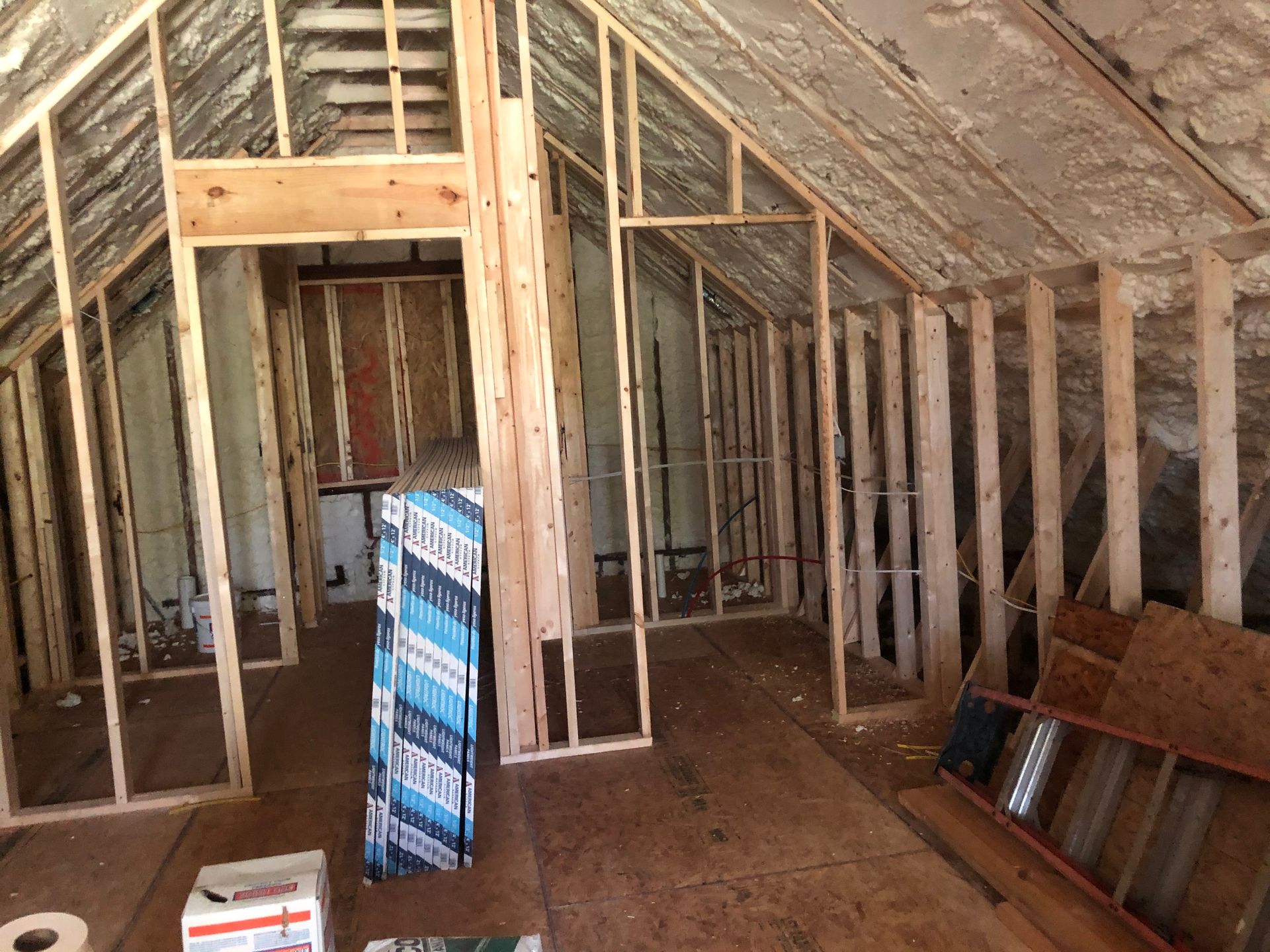 Unfinished attic framed with exposed wood beams, insulation, and construction materials on the floor.