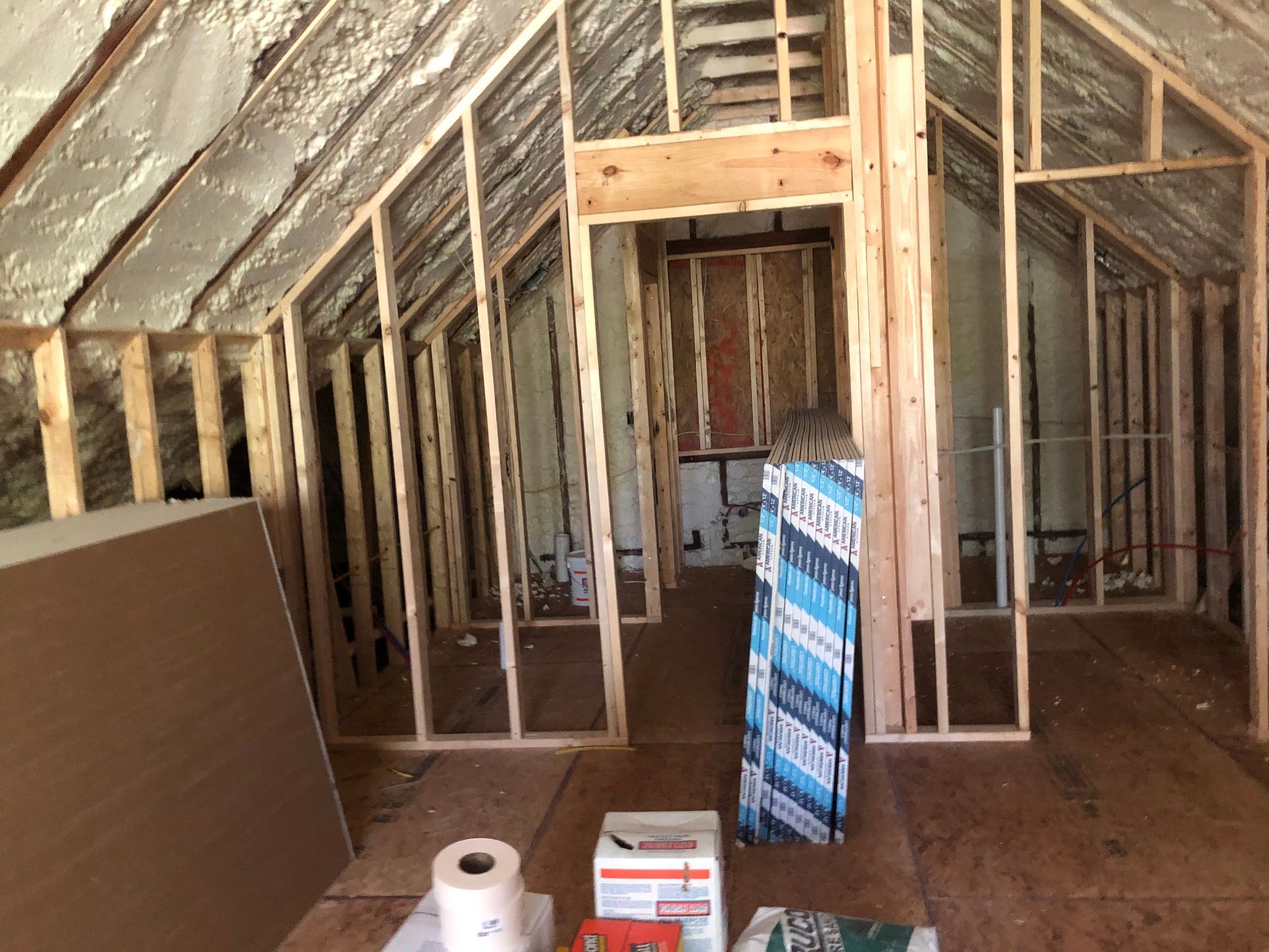Unfinished attic with exposed wooden framing, insulation, and construction materials on the floor.